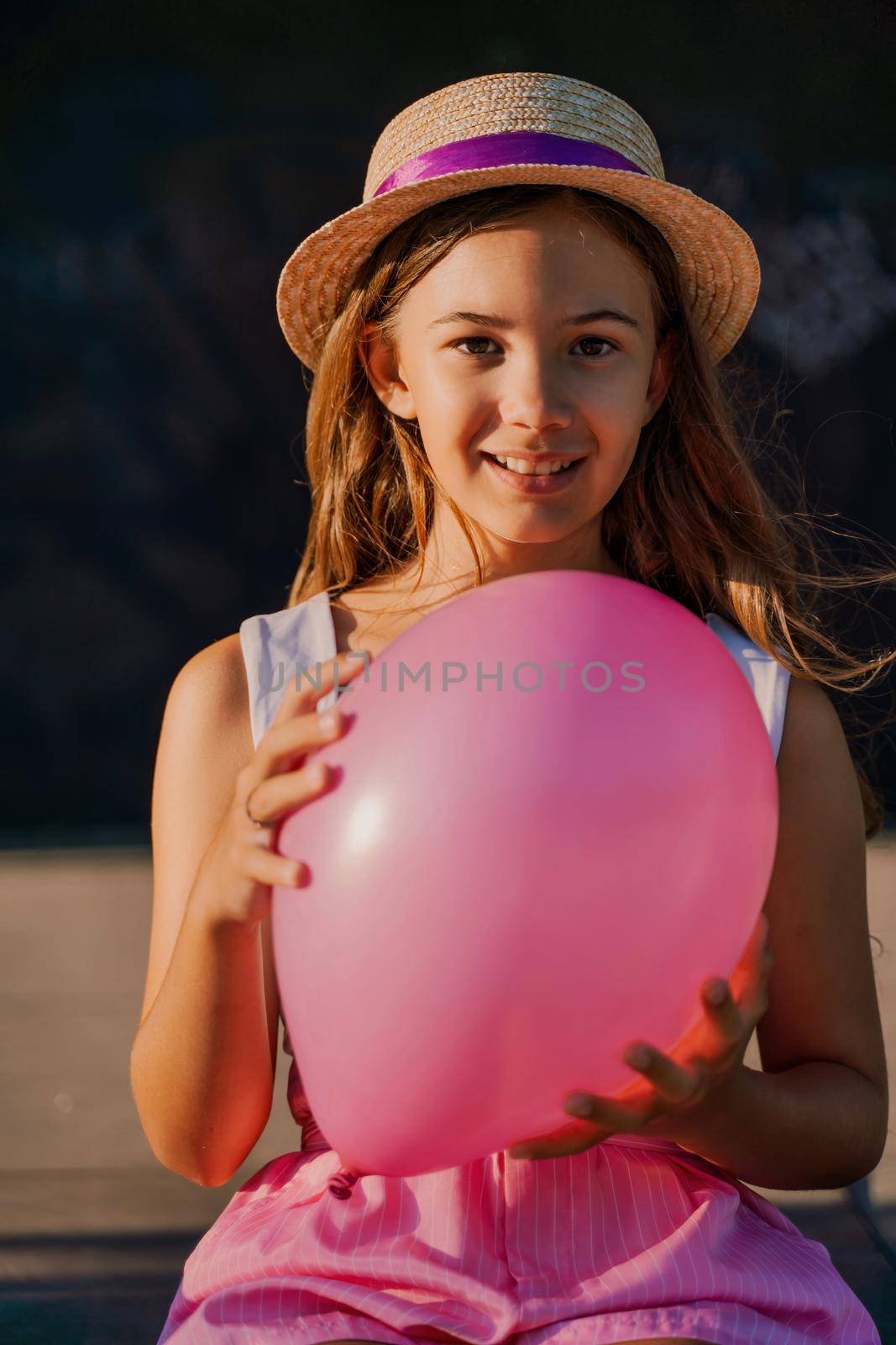 Portrait of a girl in a hat with a pink balloon. She is dressed in pink clothes and her hair is long and loose