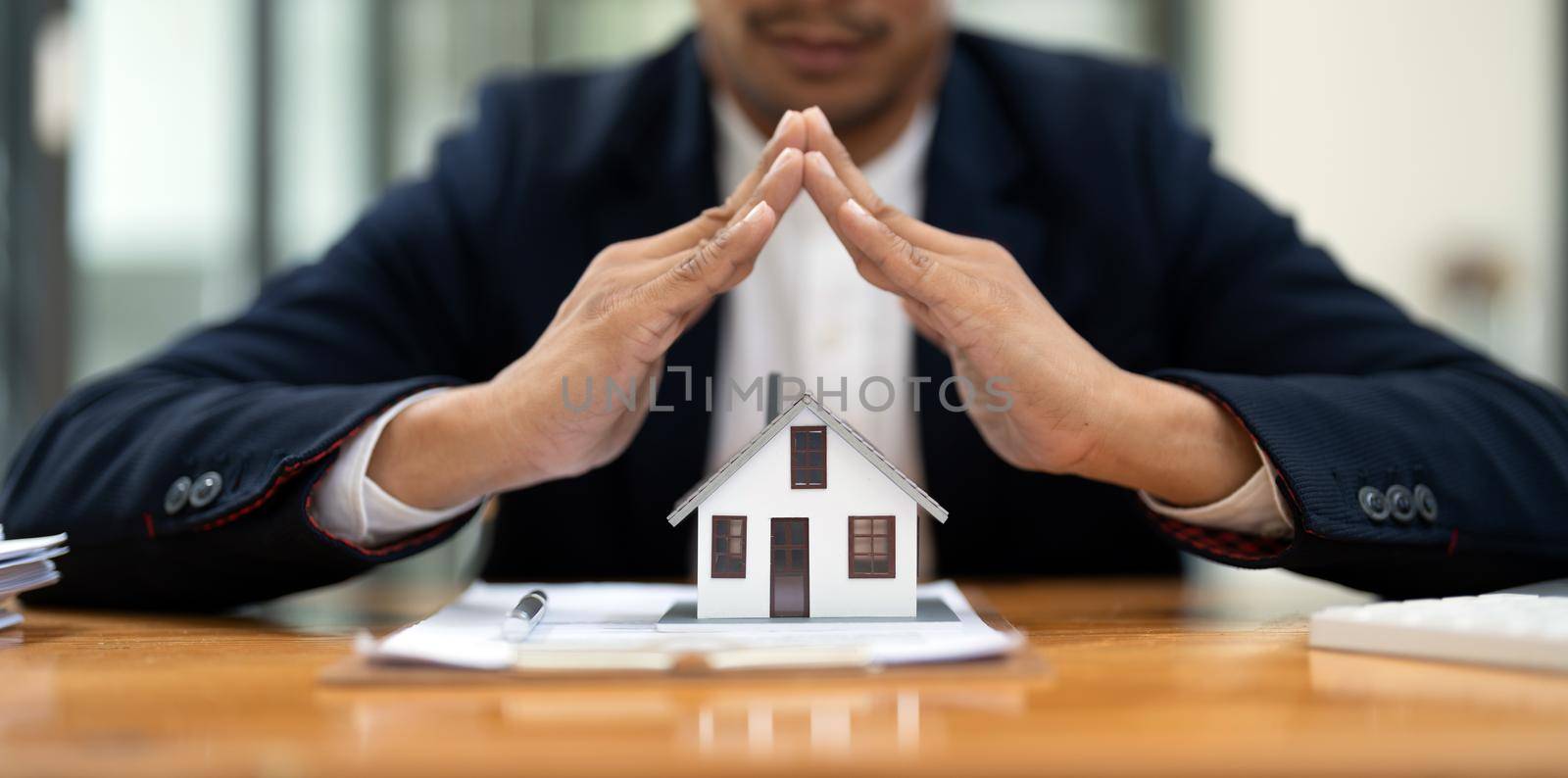Real estate concept, businessman holding protect house model. Property insurance and security concept. Protecting gesture of man and symbol of house