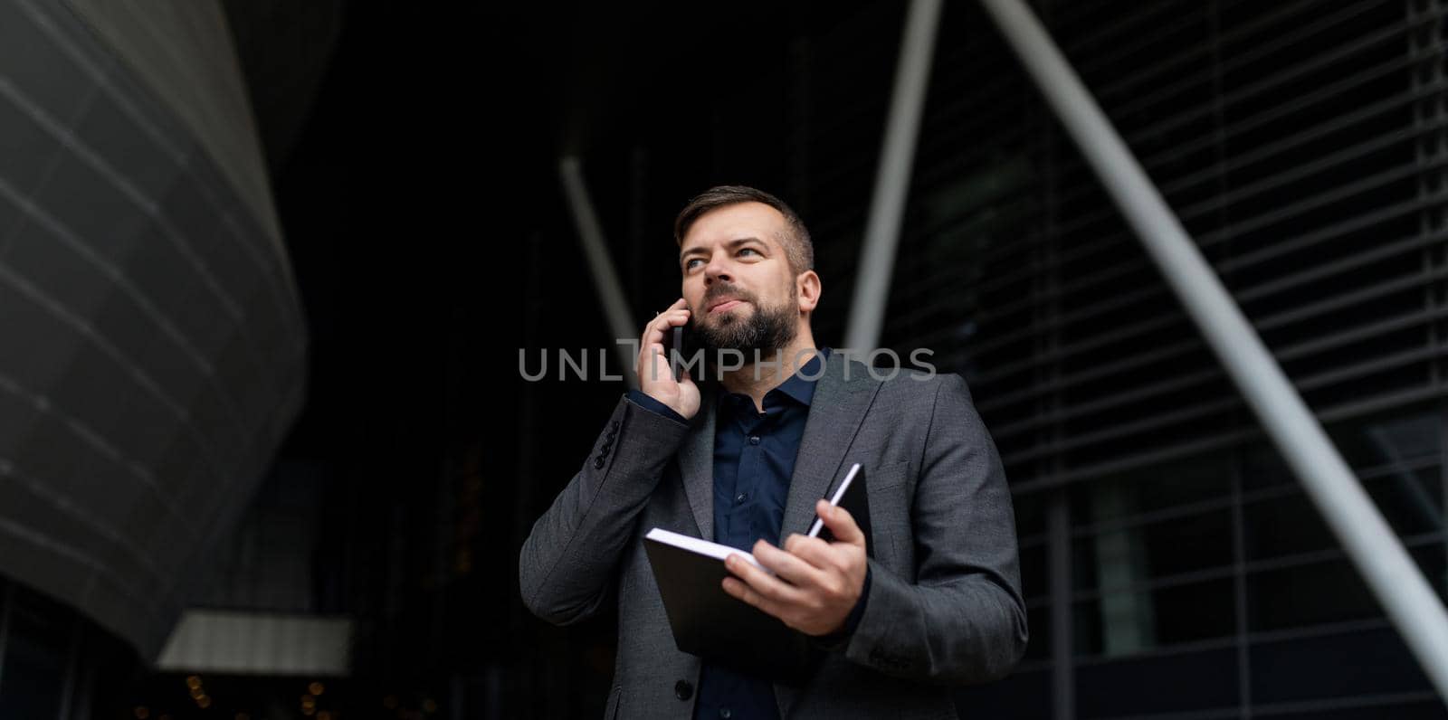 real estate agent speaks on a mobile phone with a notepad in his hands on the background of the office center.