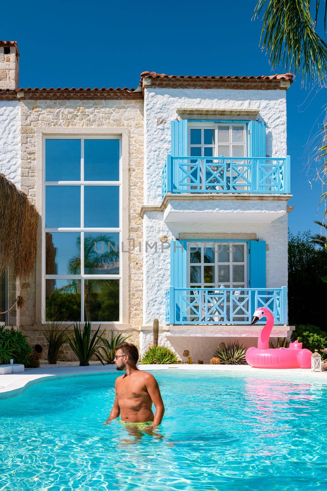 a young tanning man at a swimmingpool with red pink flamingo, pink flaming by the pool.