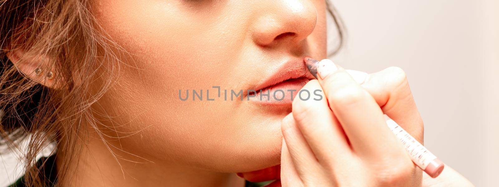 Lips makeup. Makeup artist applies contour with a pencil to the lips of a young woman in a beauty salon. by okskukuruza
