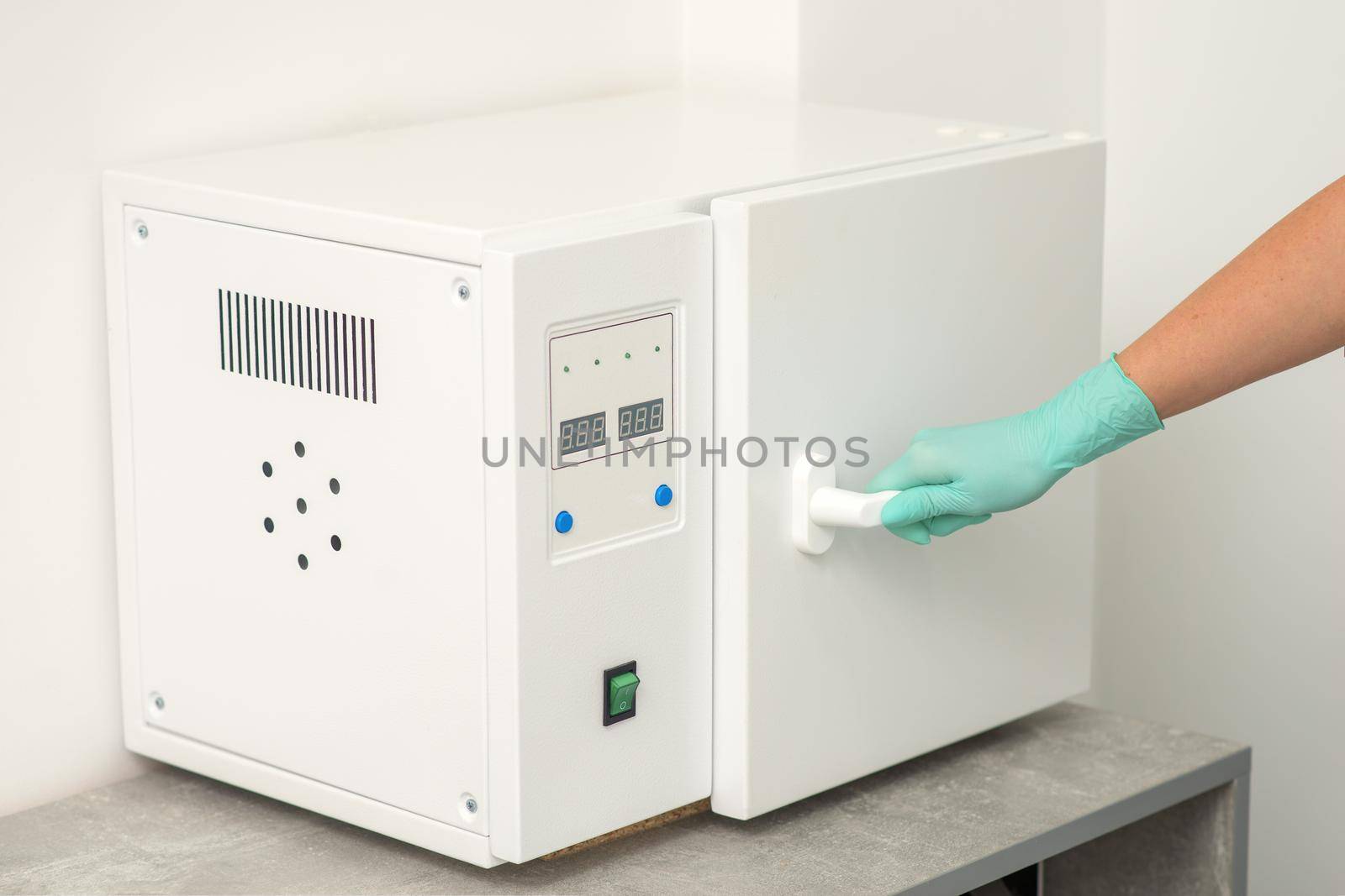 Beautician in protective gloves close the door of the machine for disinfection of tools before the medical procedures