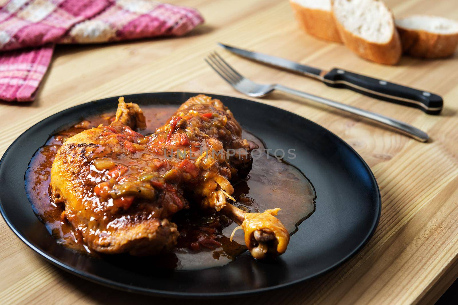 traditional dish of chicken with vegetables in sauce. On the wooden table there are cutlery, bread and a vintage kitchen rag