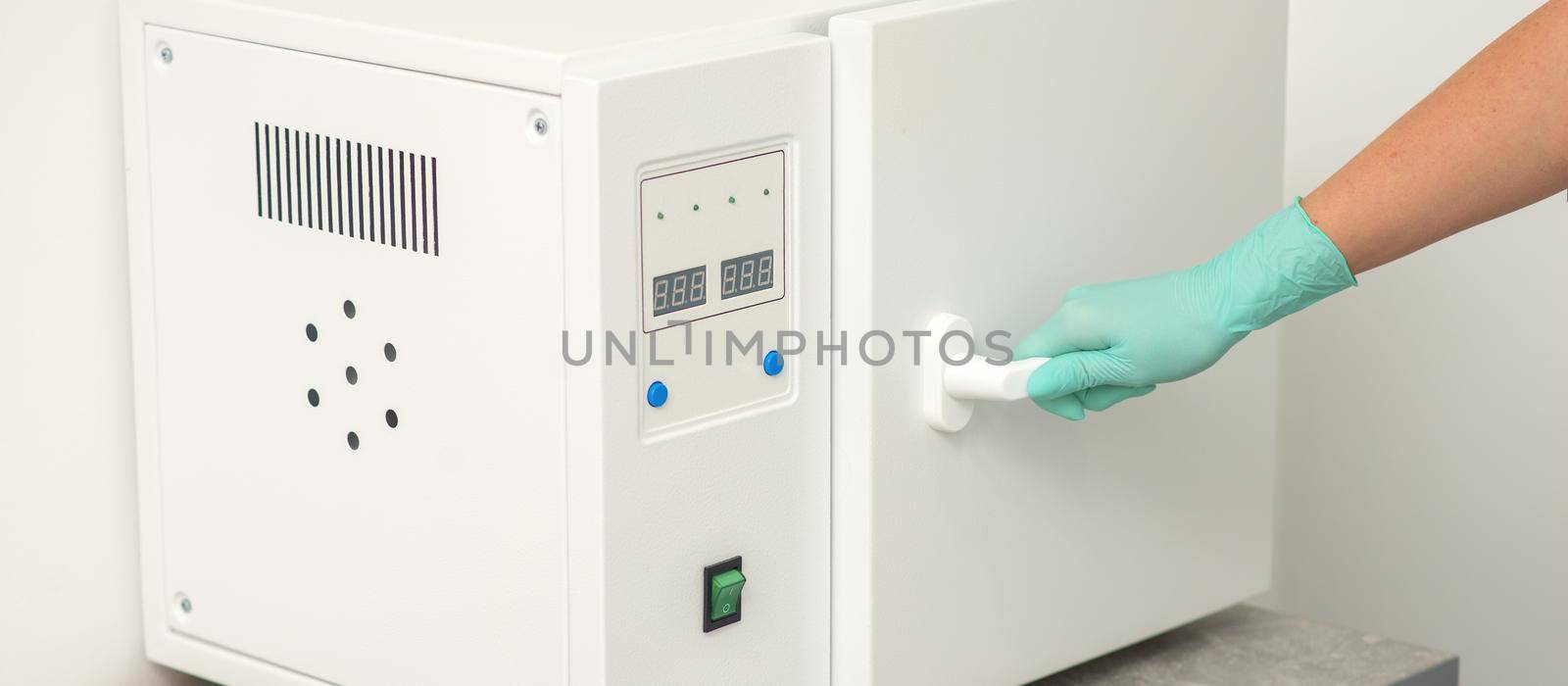 Beautician in protective gloves close the door of the machine for disinfection of tools before the medical procedures