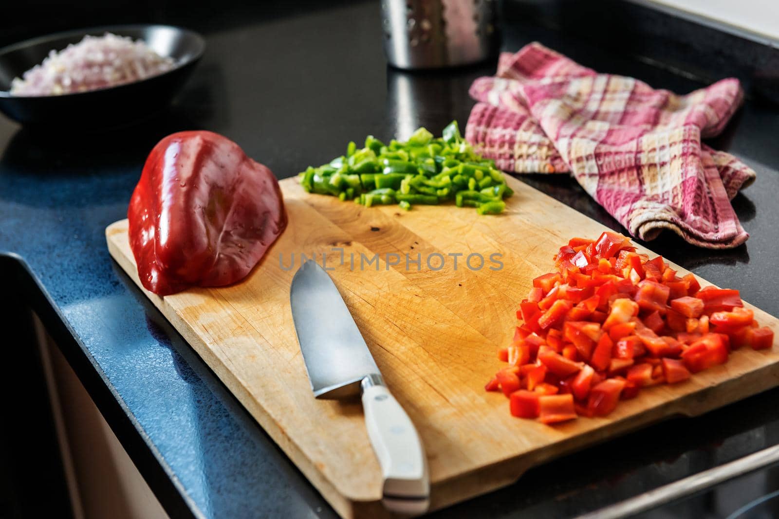 old wooden cutting board with a chef's knife, chopped red and green pepper, a red pepper cut in half and a napkin