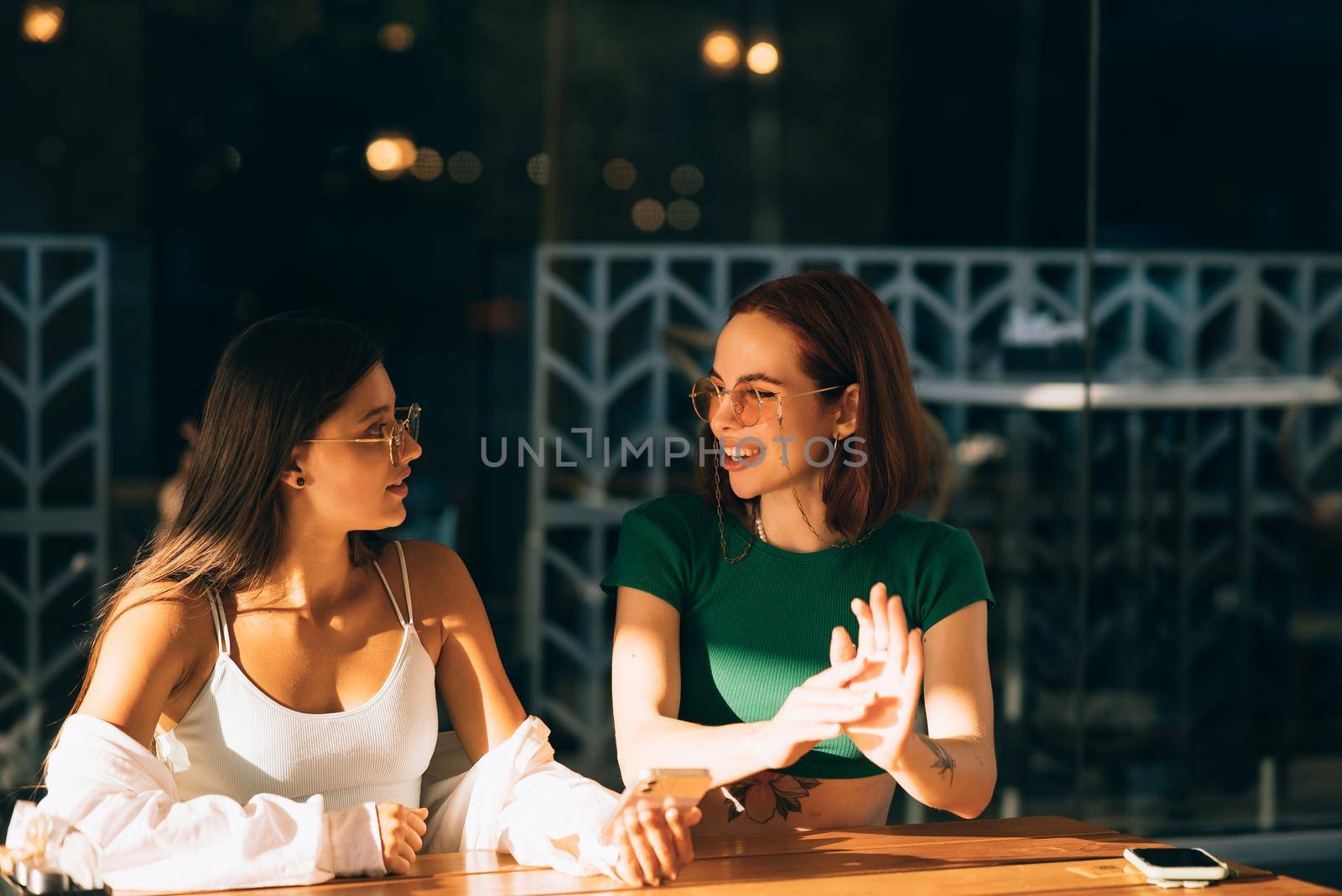 Two excited young girls using mobile phones while sitting at the cafe outdoors