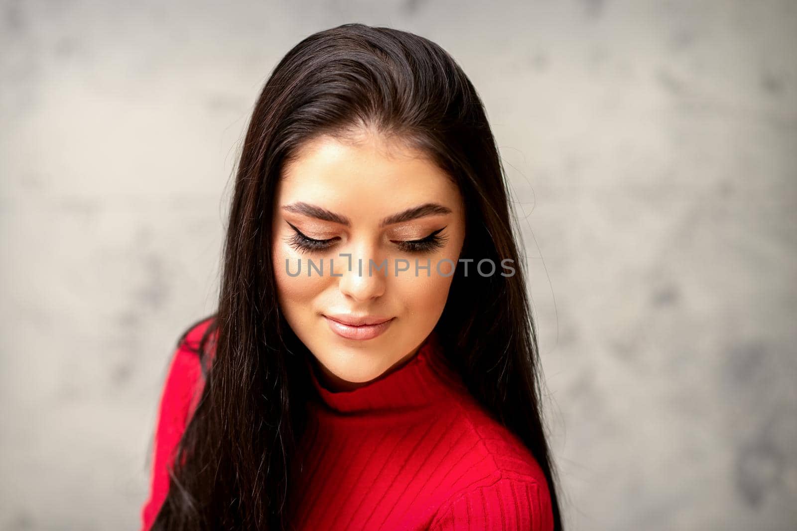 The fashionable young woman. Portrait of the beautiful female model with long hair and makeup with eyelash extensions. Beauty young woman with a black hairstyle on the background of a gray wall