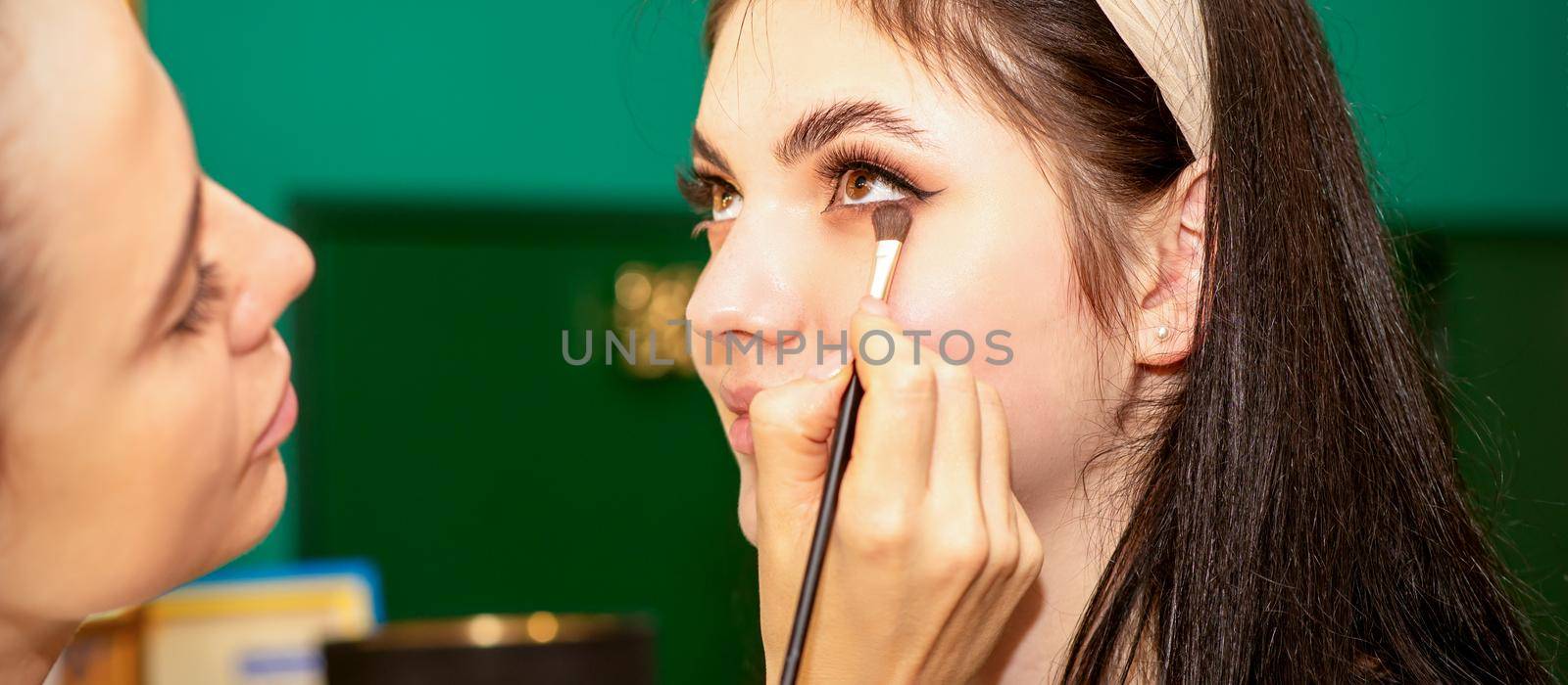 Make-up in the process. The hand of the makeup artist applies eye shadow under the eyes of a young beautiful caucasian model woman