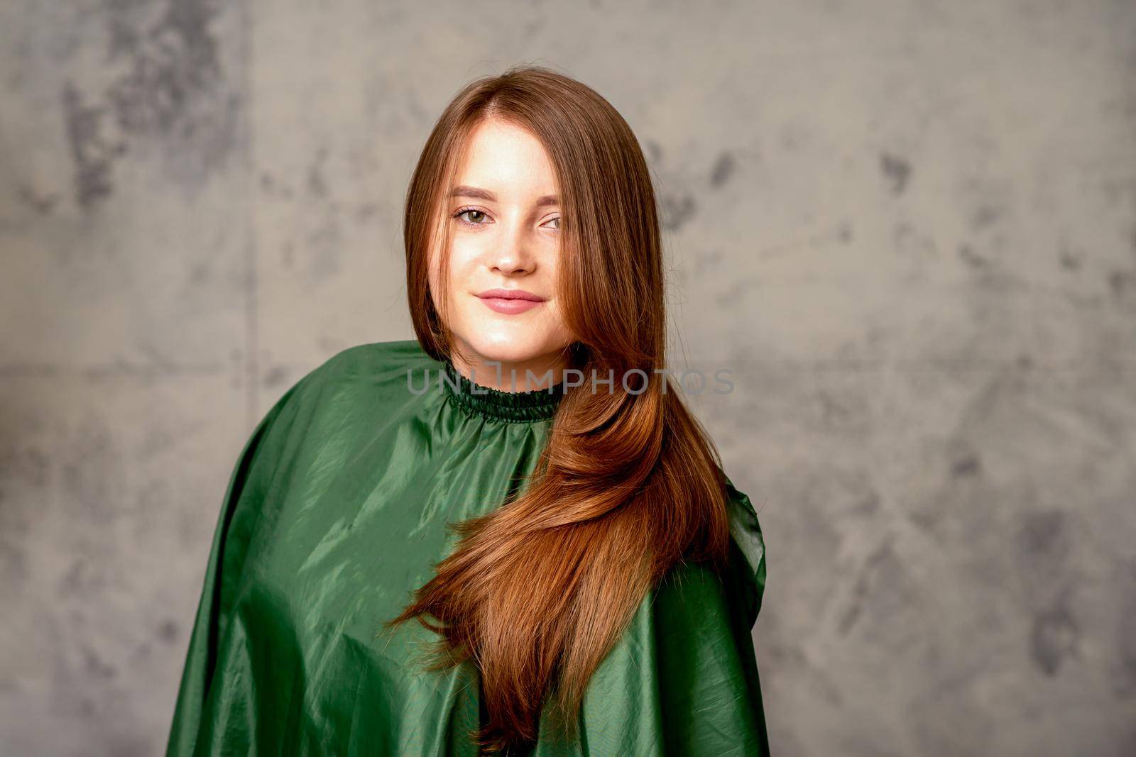 The fashionable young woman. Portrait of the beautiful female model with long hair and makeup. Beauty young caucasian woman with a brown curly hairstyle on the background of a gray wall