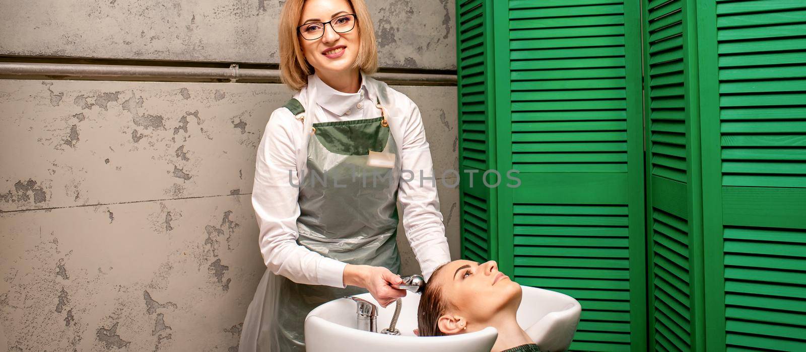 Portrait of female hairdresser washing hair of the young caucasian woman in a beauty salon. by okskukuruza