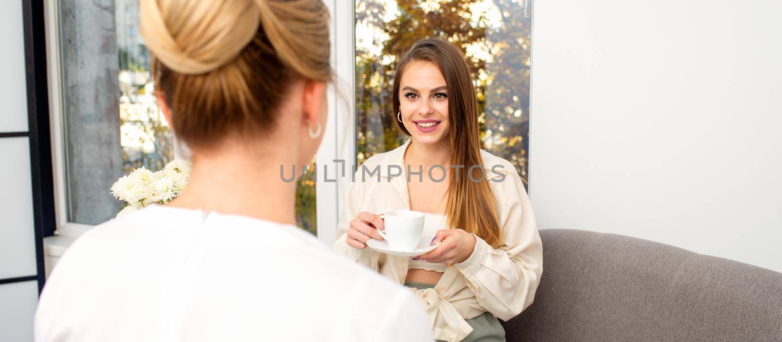 The young caucasian woman with a cup of coffee has an appointment with a female doctor beautician in the hospital office. by okskukuruza