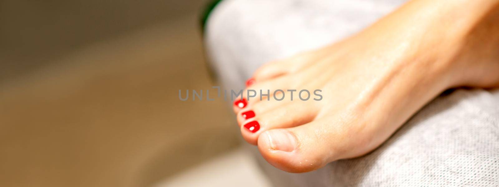 Nail painting process. Red painted fingernails on a female leg in a beauty salon, closeup