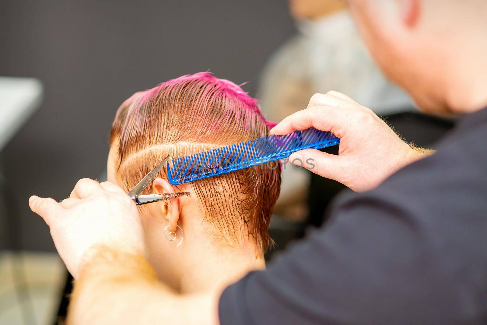 Haircut of dyed short pink wet hair of young caucasian woman by a male hairdresser in a barbershop
