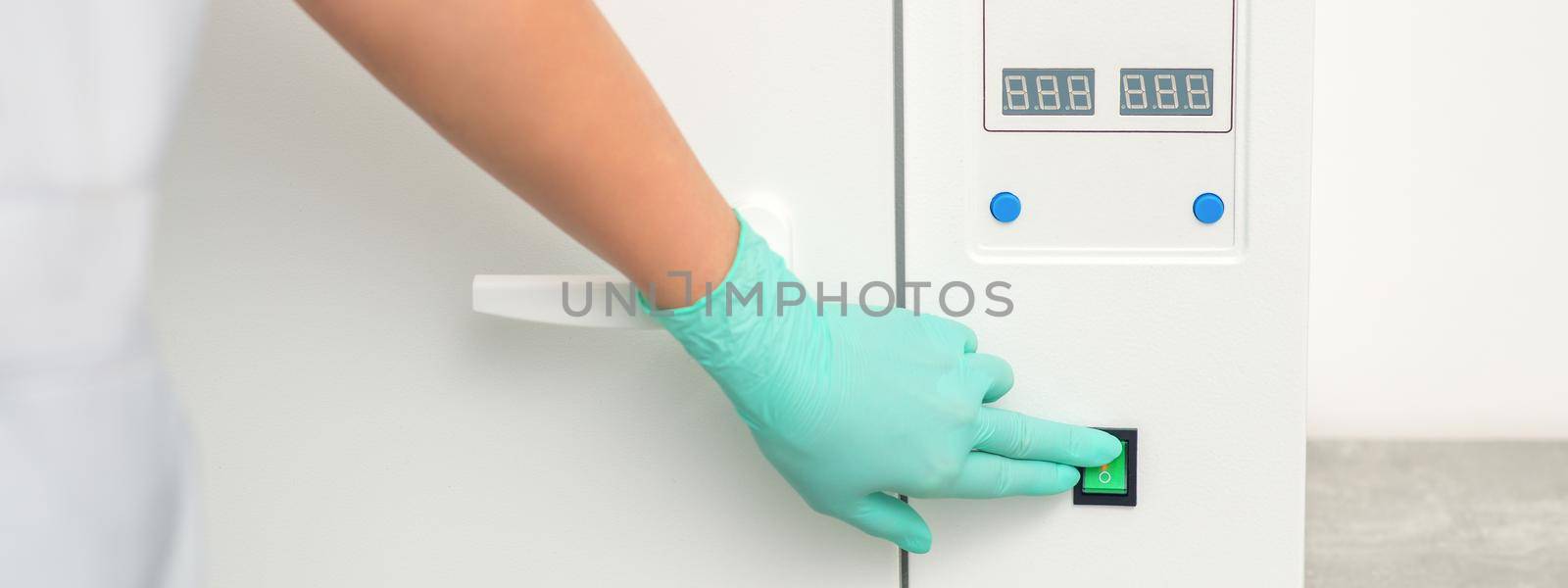 Beautician in protective gloves starts the machine for disinfection of tools before the medical procedure. by okskukuruza