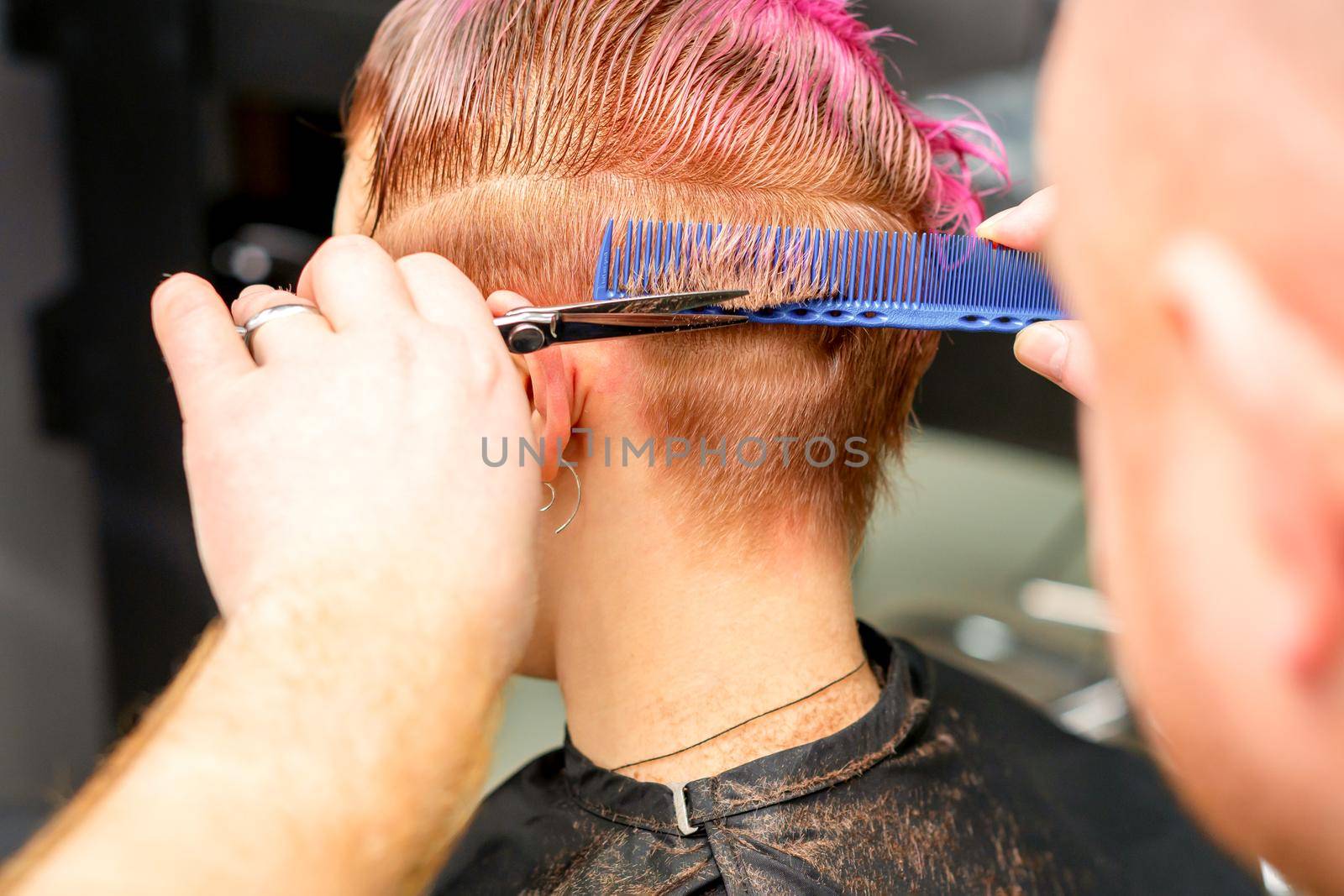 Haircut of dyed short pink wet hair of young caucasian woman by a male hairdresser in a barbershop