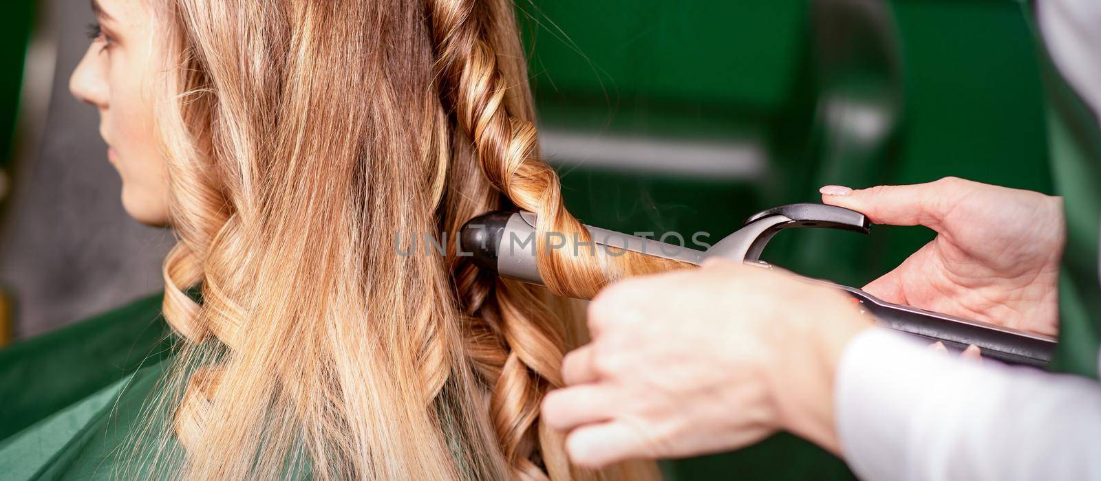 The female hairdresser is curling hair for a brown-haired young caucasian woman in a beauty salon