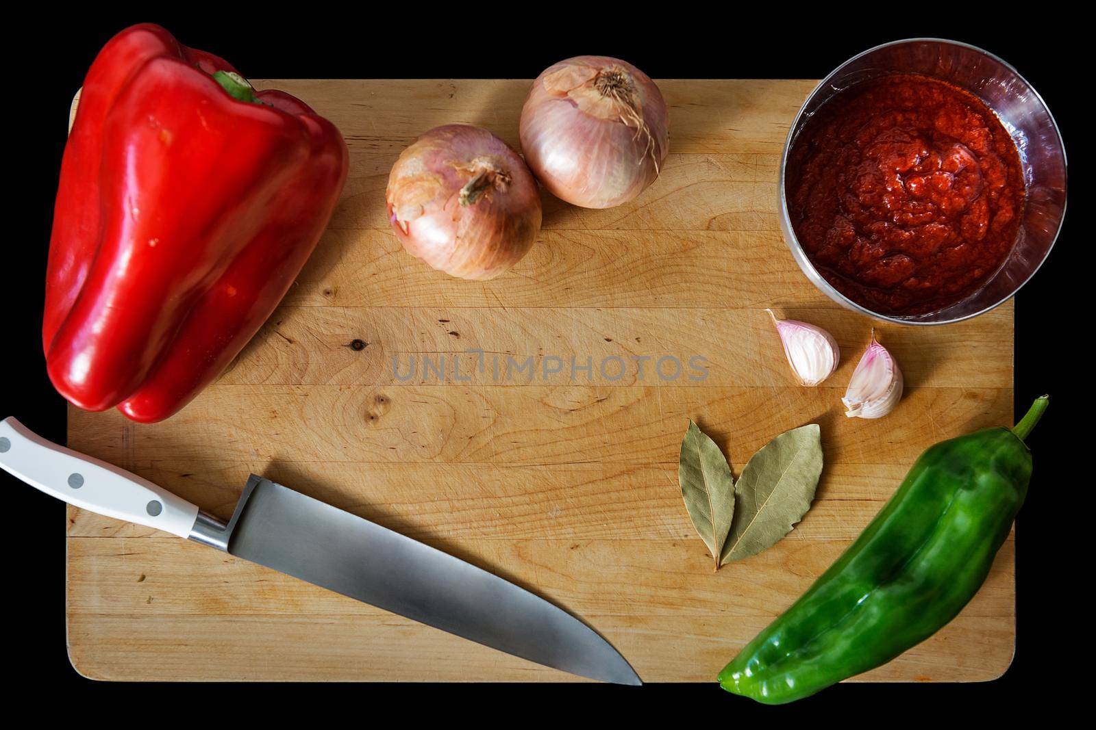 wooden cutting board with peppers, onions, garlic, bay leaves, tomato sauce in a bowl and a chef's knife. Top view with copy space