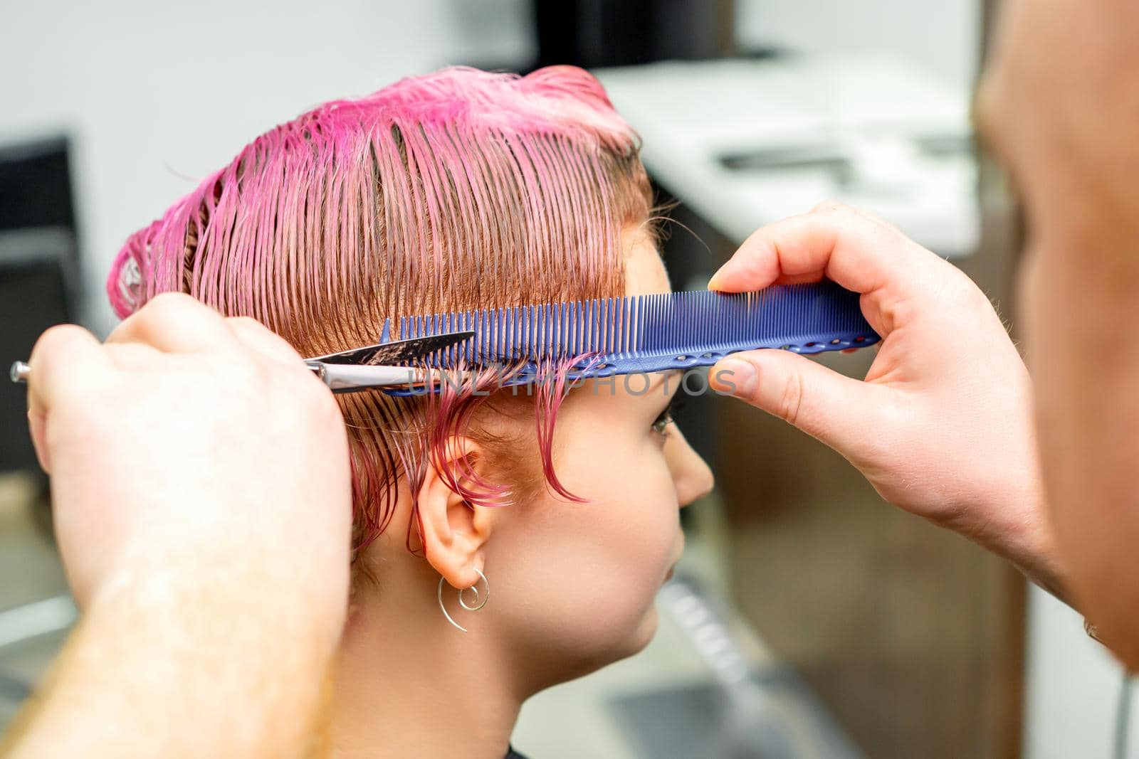 Haircut of dyed short pink wet hair of young caucasian woman by a male hairdresser in a barbershop