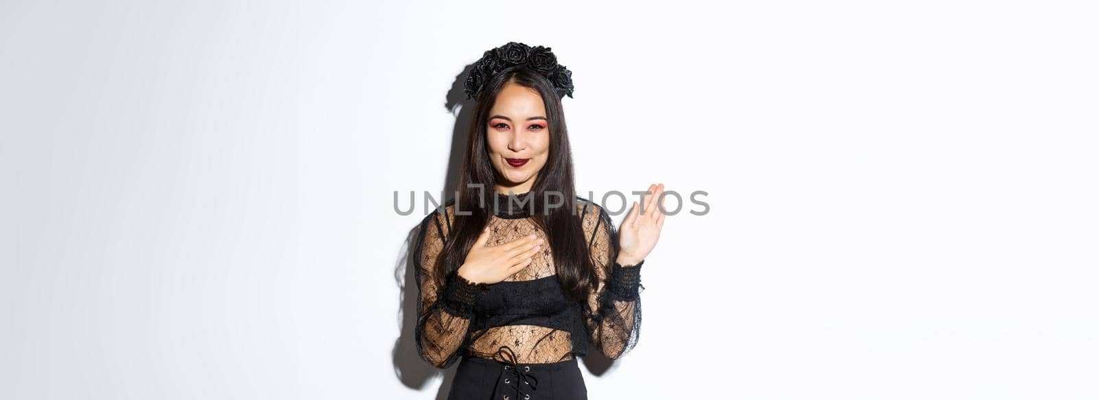 Image of smiling beautiful woman making promise, give oath on her heart, raising one arm and looking at camera sincere, standing over white background by Benzoix