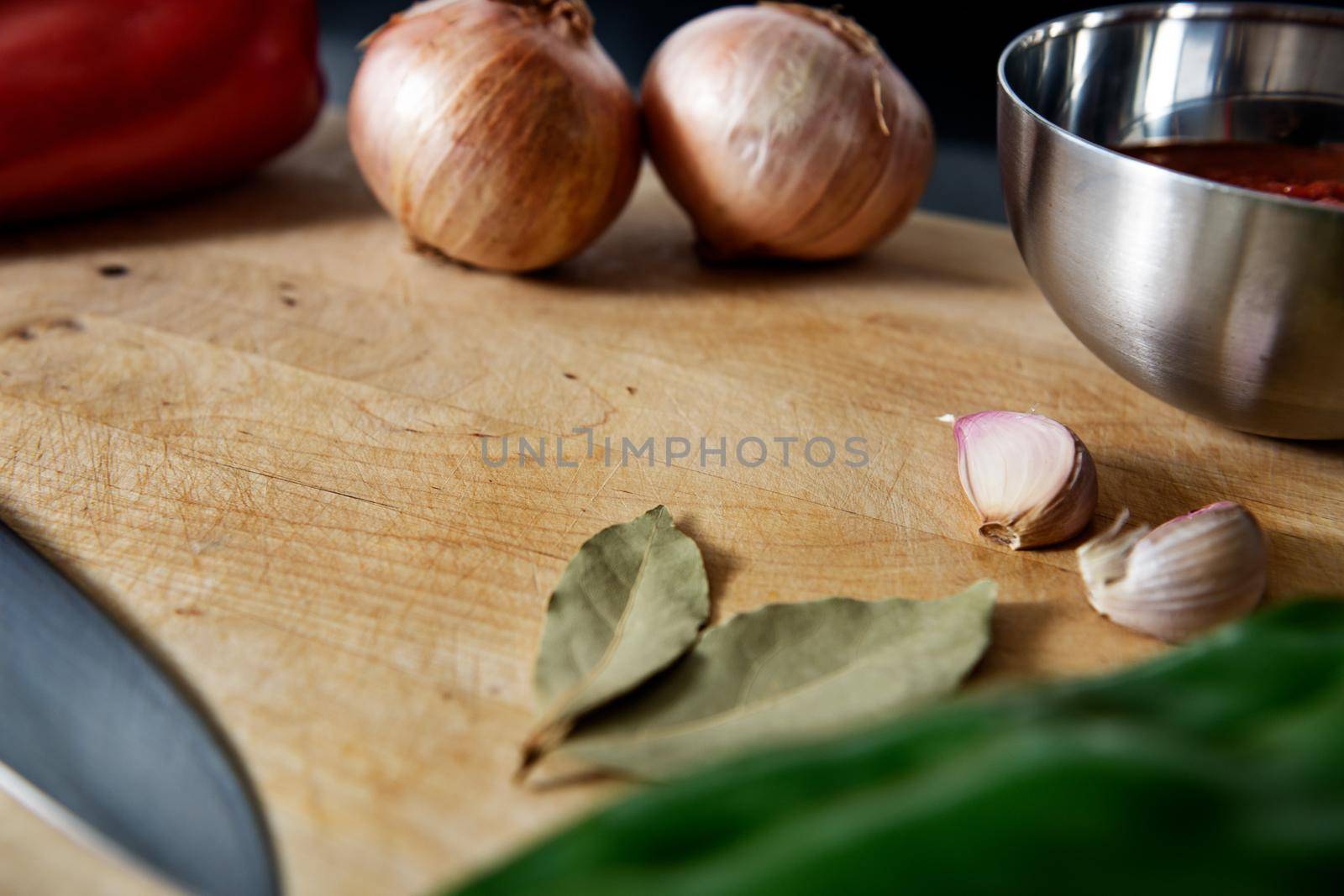 wooden cutting board with peppers, onions, garlic, bay leaves, tomato sauce in a bowl and a chef's knife. Closeup with lens blur and copy space