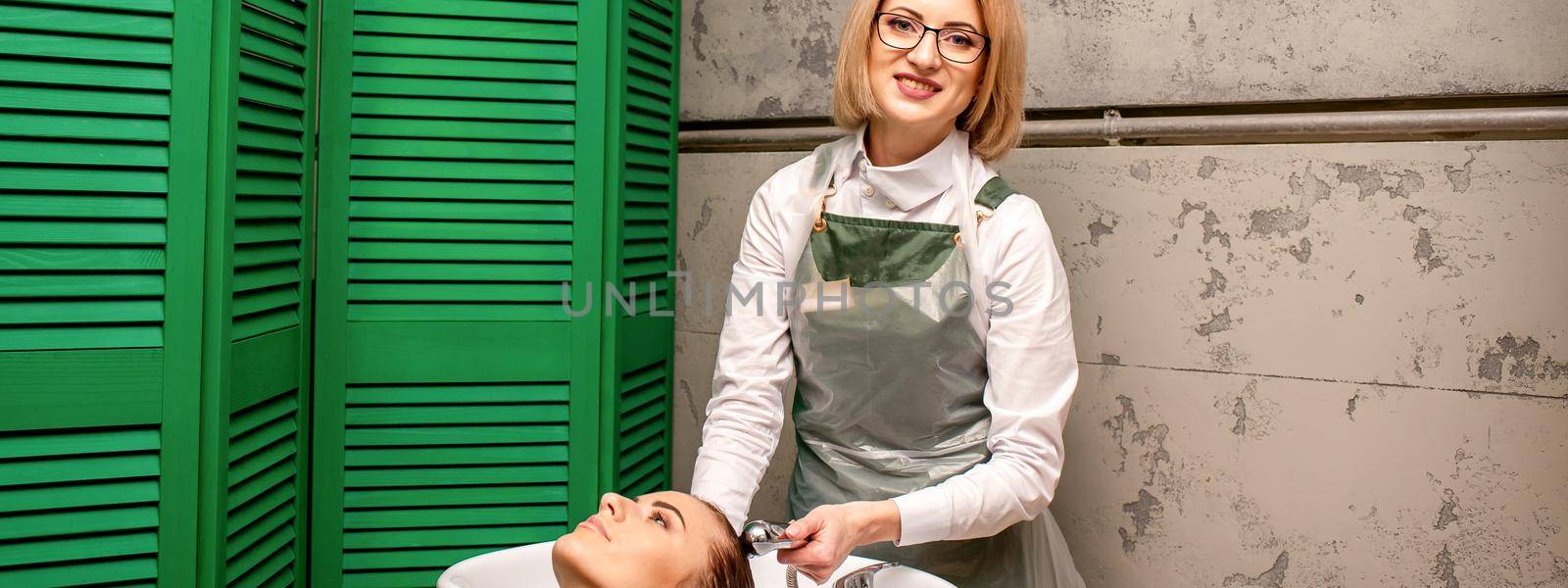 Portrait of female hairdresser washing hair of the young caucasian woman in a beauty salon. by okskukuruza