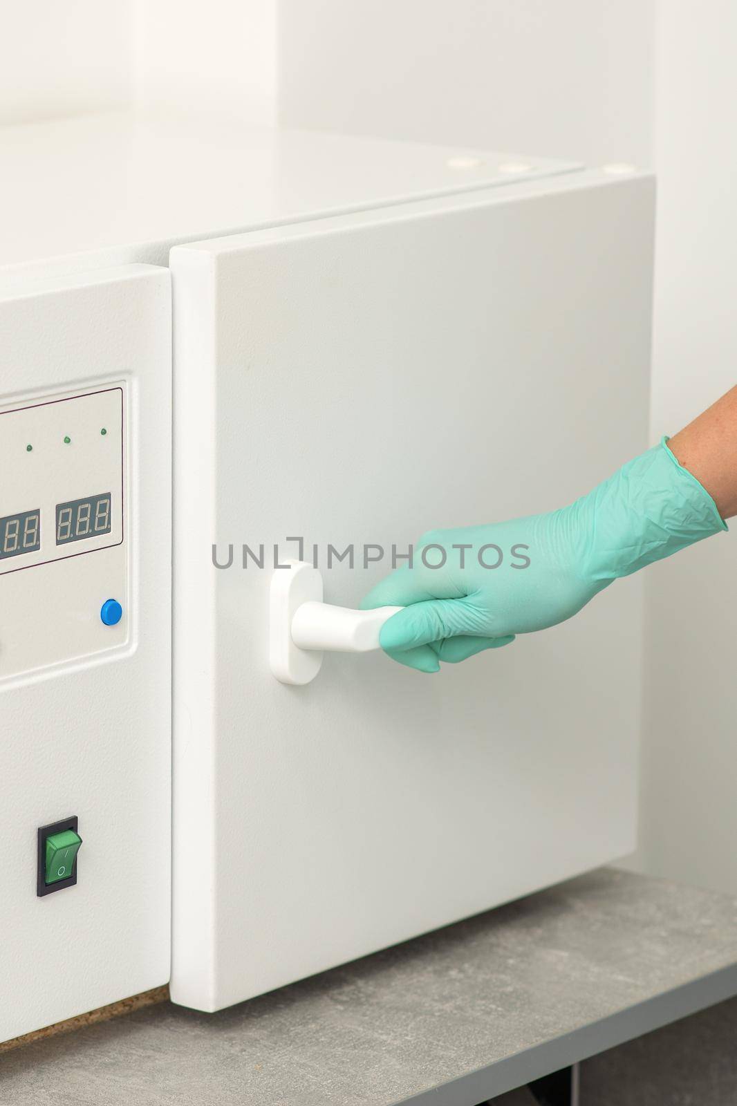 Beautician in protective gloves close the door of the machine for disinfection of tools before the medical procedures