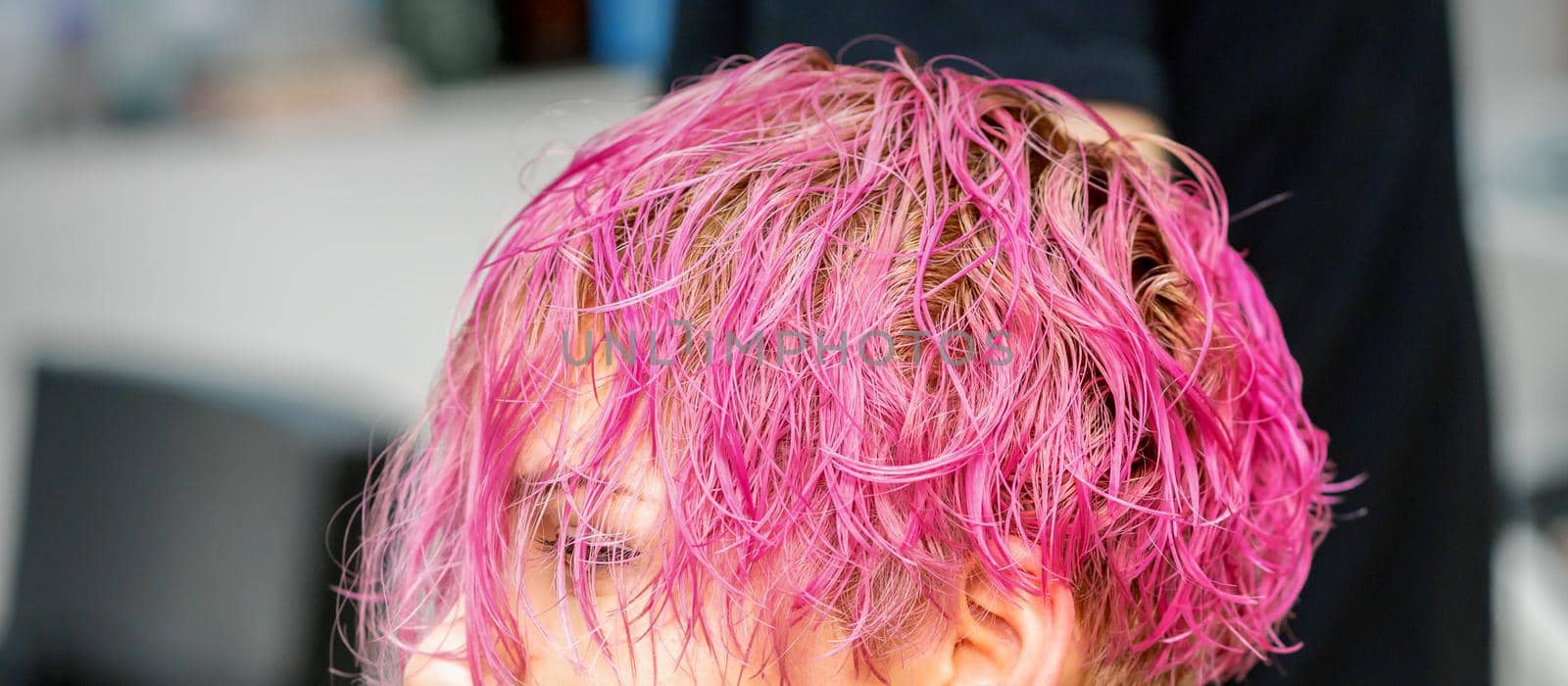 Beautiful young caucasian woman receiving new short pink hairstyle in hairdresser salon. by okskukuruza