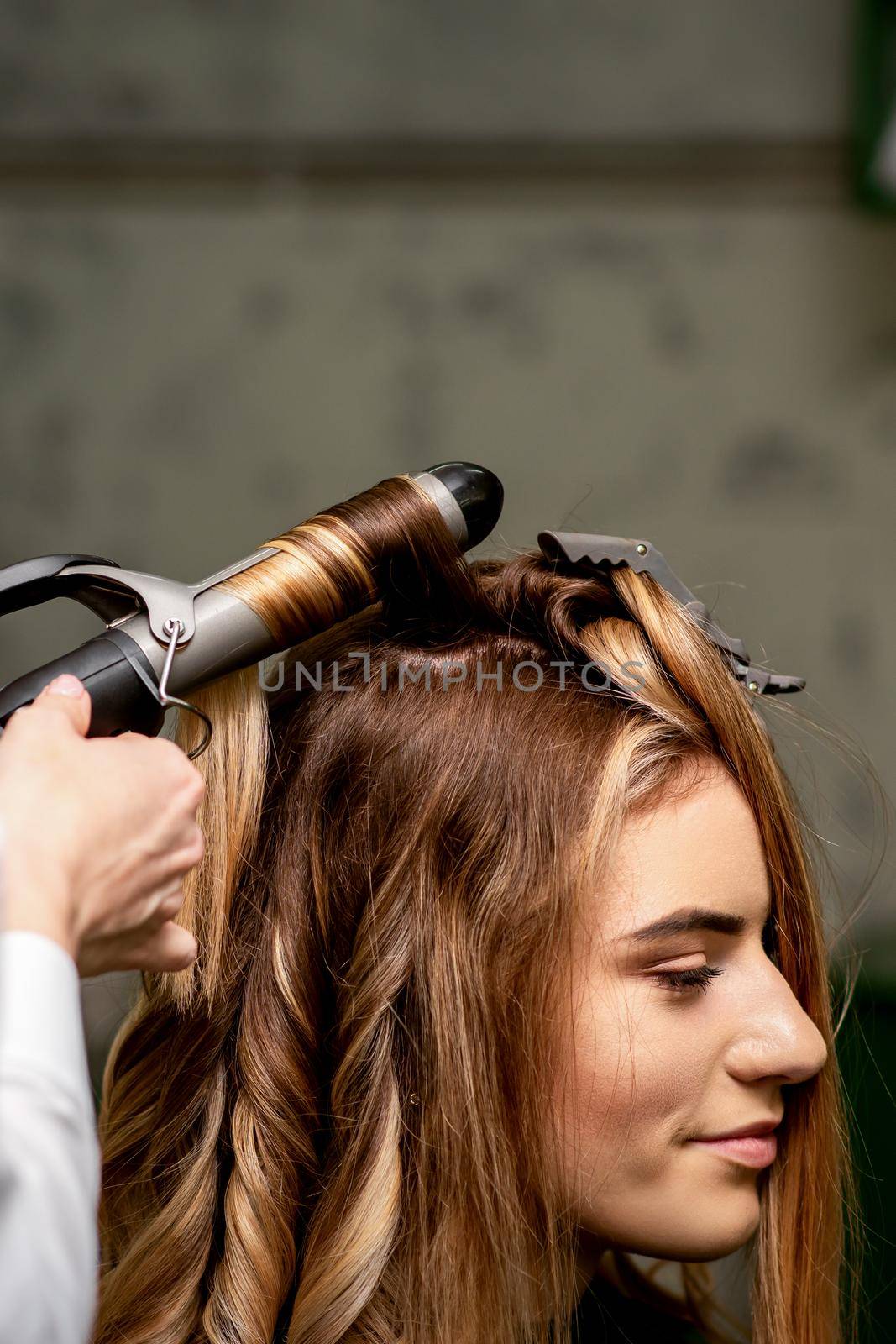 The female hairdresser is curling hair for a brown-haired young caucasian woman in a beauty salon. by okskukuruza