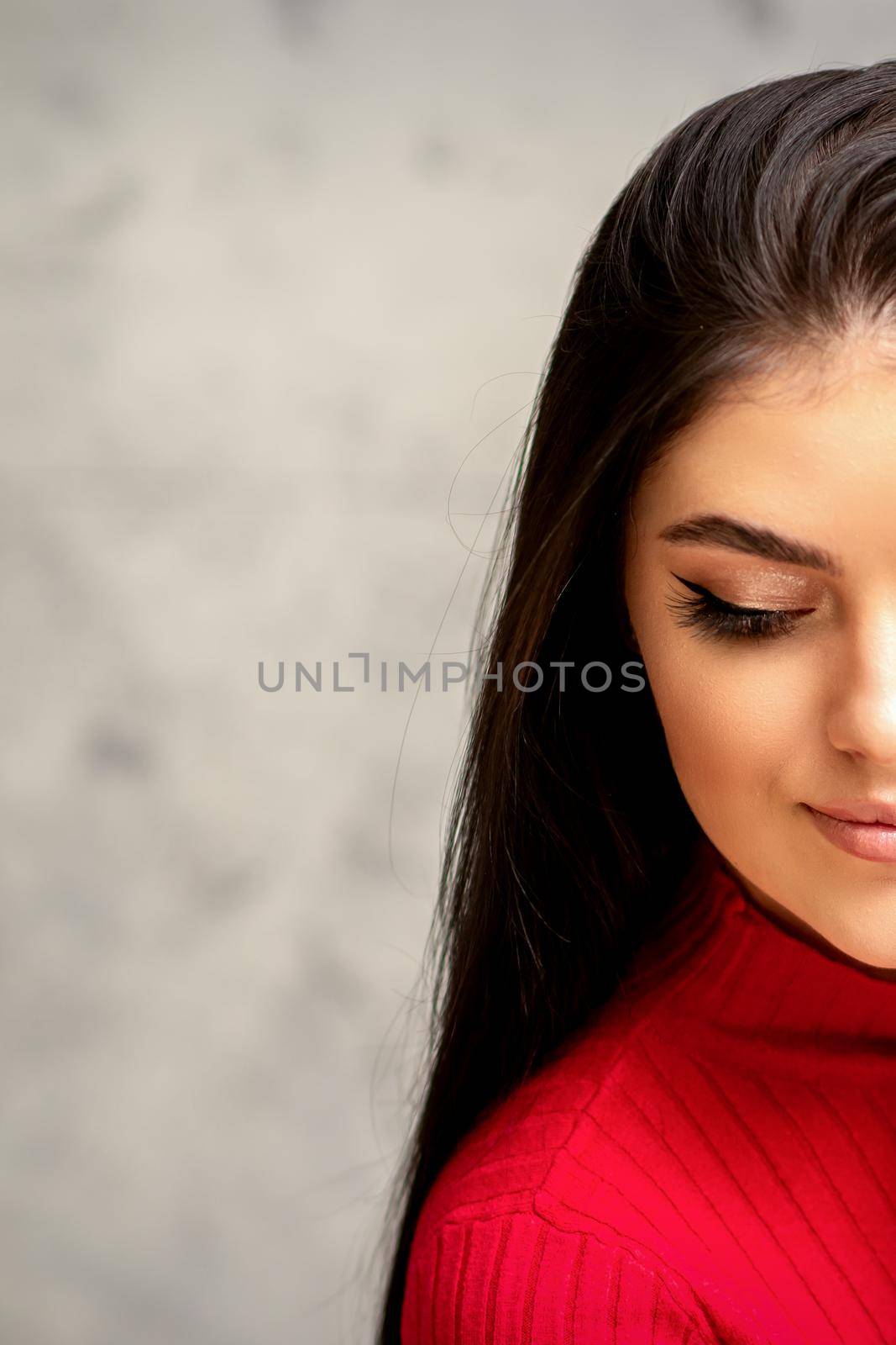 The fashionable young woman. Portrait of the beautiful female model with long hair and makeup with eyelash extensions. Beauty young woman with a black hairstyle on the background of a gray wall