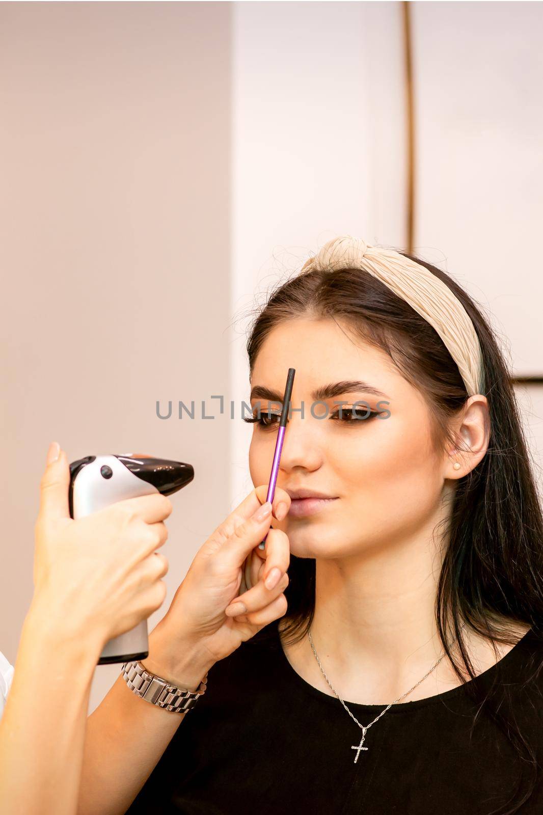 Makeup artist using an airbrush on the face of a young caucasian woman in a beauty salon. by okskukuruza