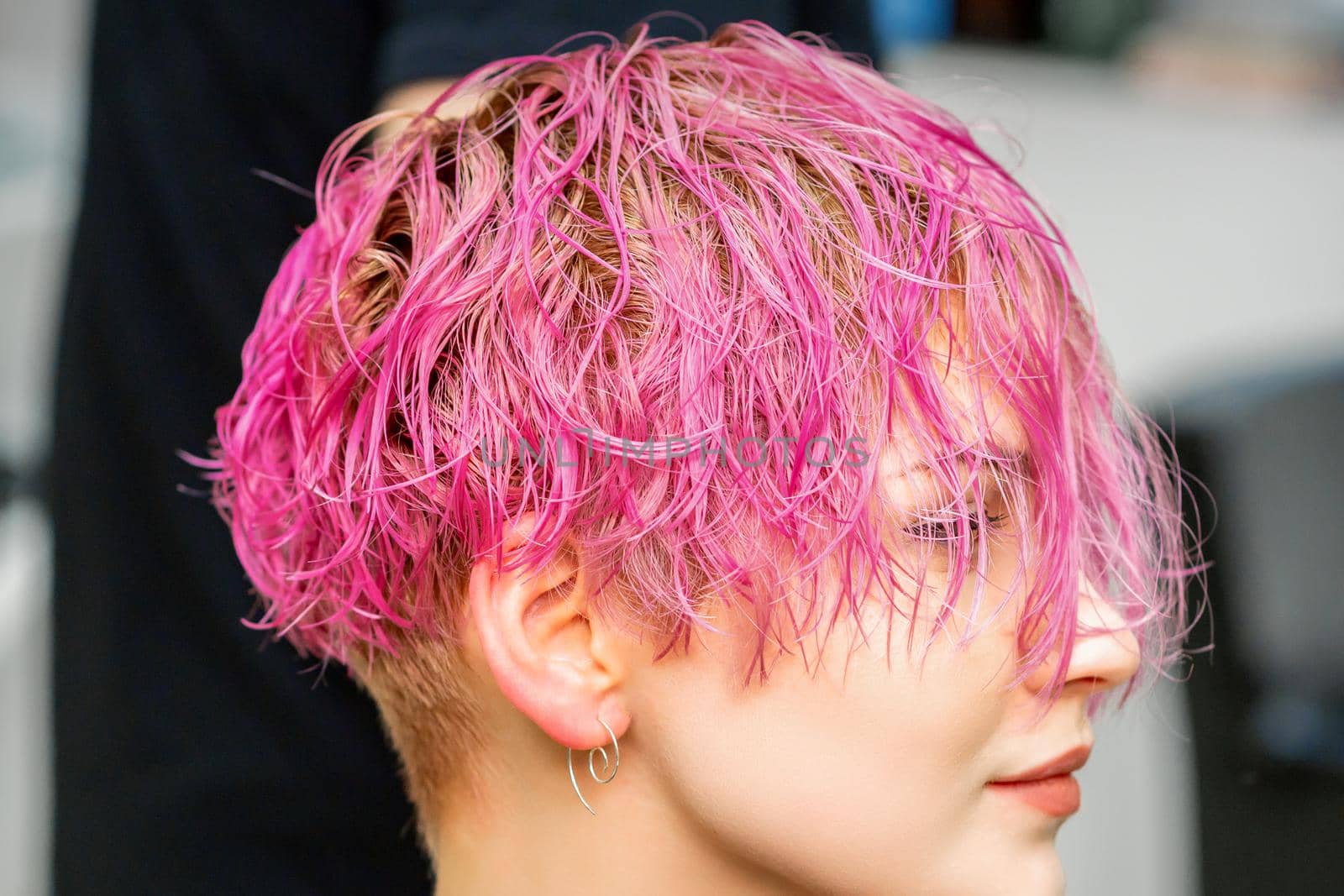 Beautiful young caucasian woman receiving new short pink hairstyle in hairdresser salon