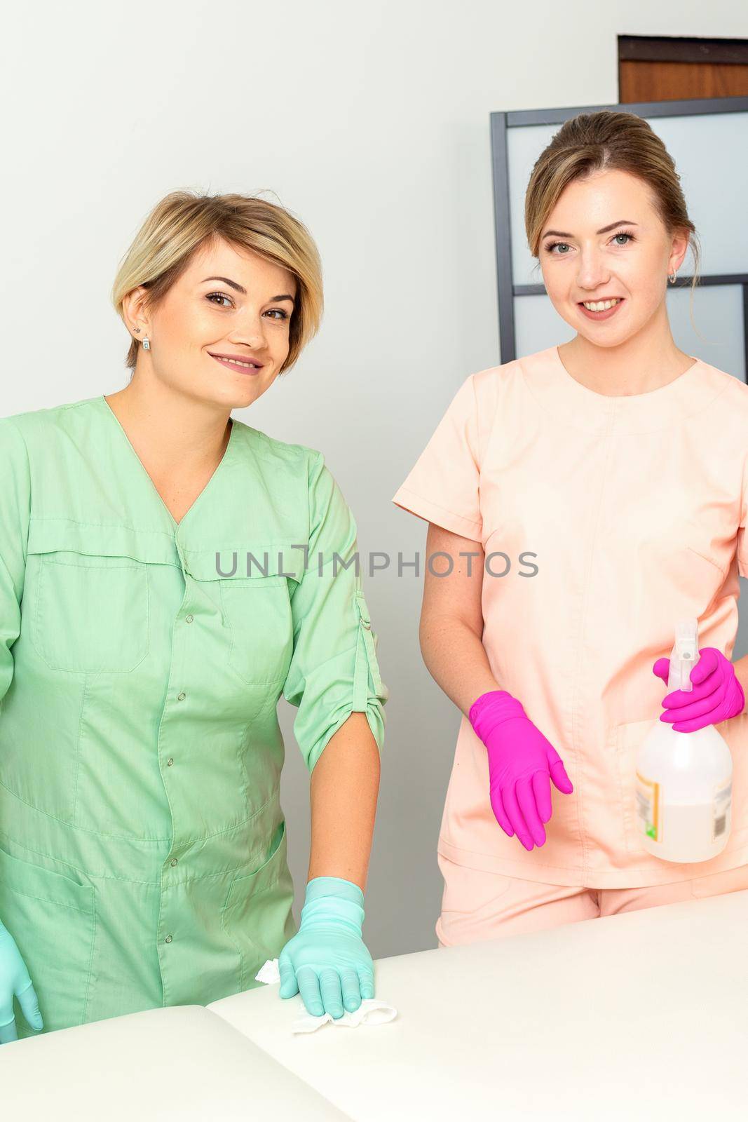 Two medical workers disinfect the patient's couch with sanitizer spray and a clean napkin. Health and hygiene concept. by okskukuruza