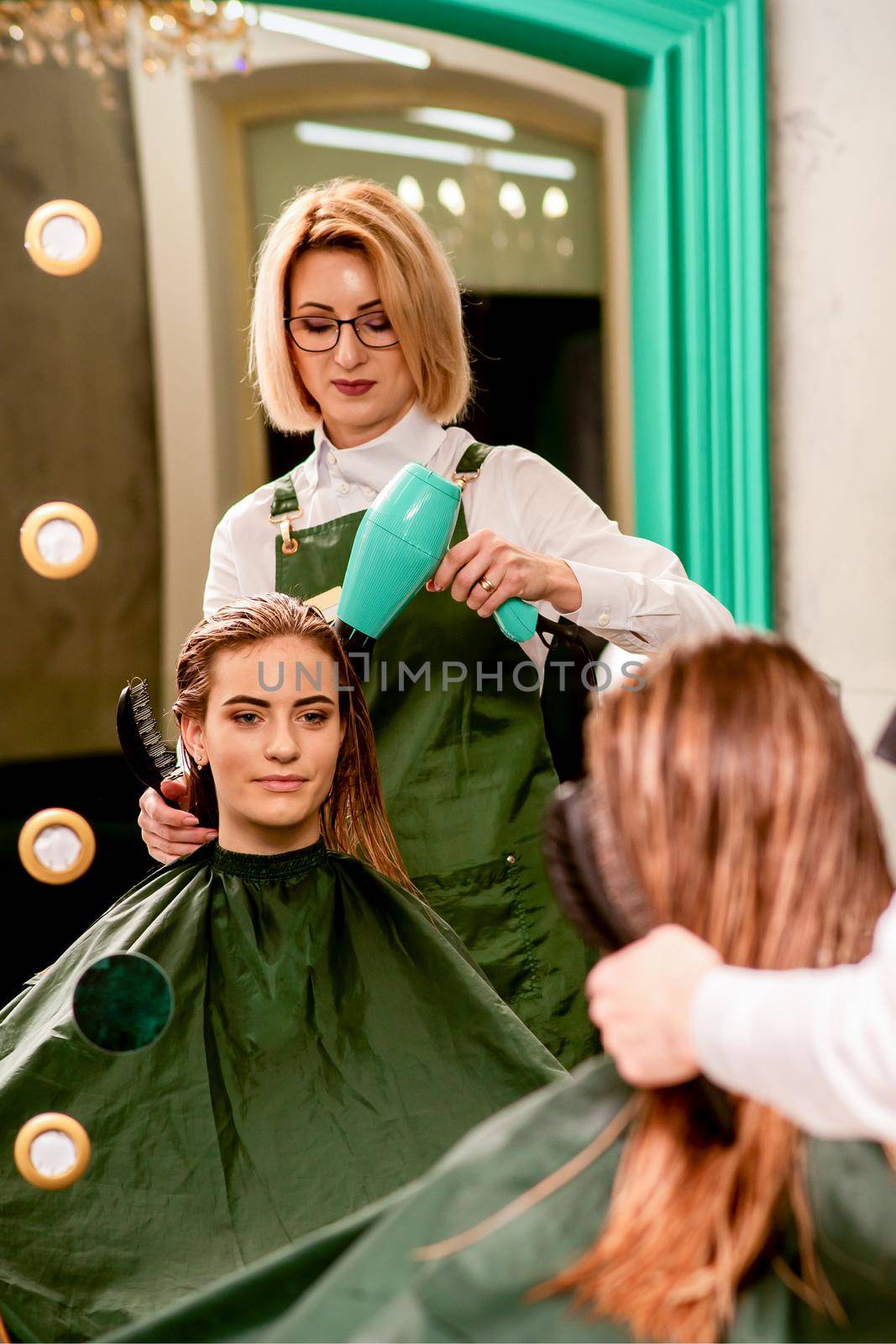 The hairdresser dries hair with a hairdryer of the beautiful young caucasian woman in the beauty salon. by okskukuruza