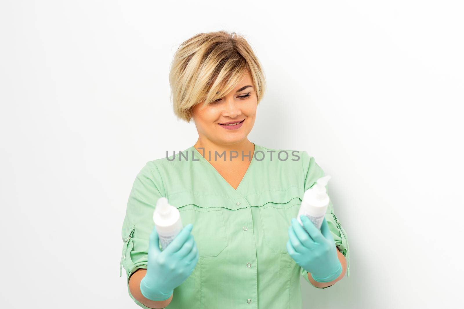 Cosmetics creams and skin care products in the hands of the female beautician smiling and standing over the white wall background