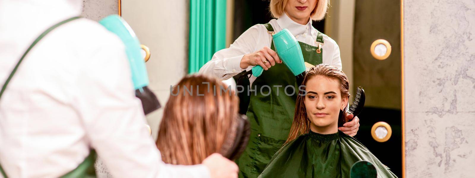 The hairdresser dries hair with a hairdryer of the beautiful young caucasian woman in the beauty salon