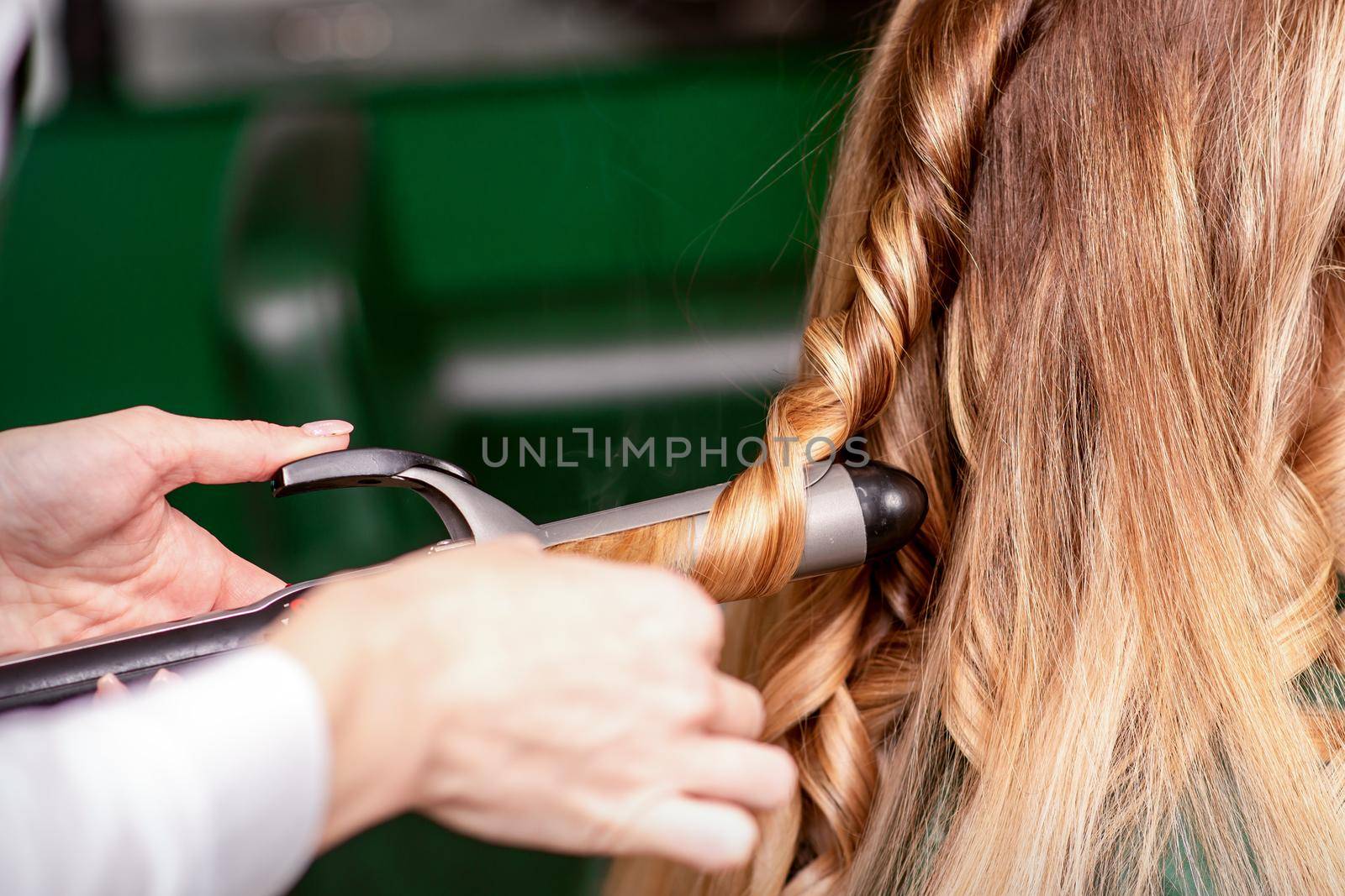 The female hairdresser is curling hair for a brown-haired young caucasian woman in a beauty salon. by okskukuruza