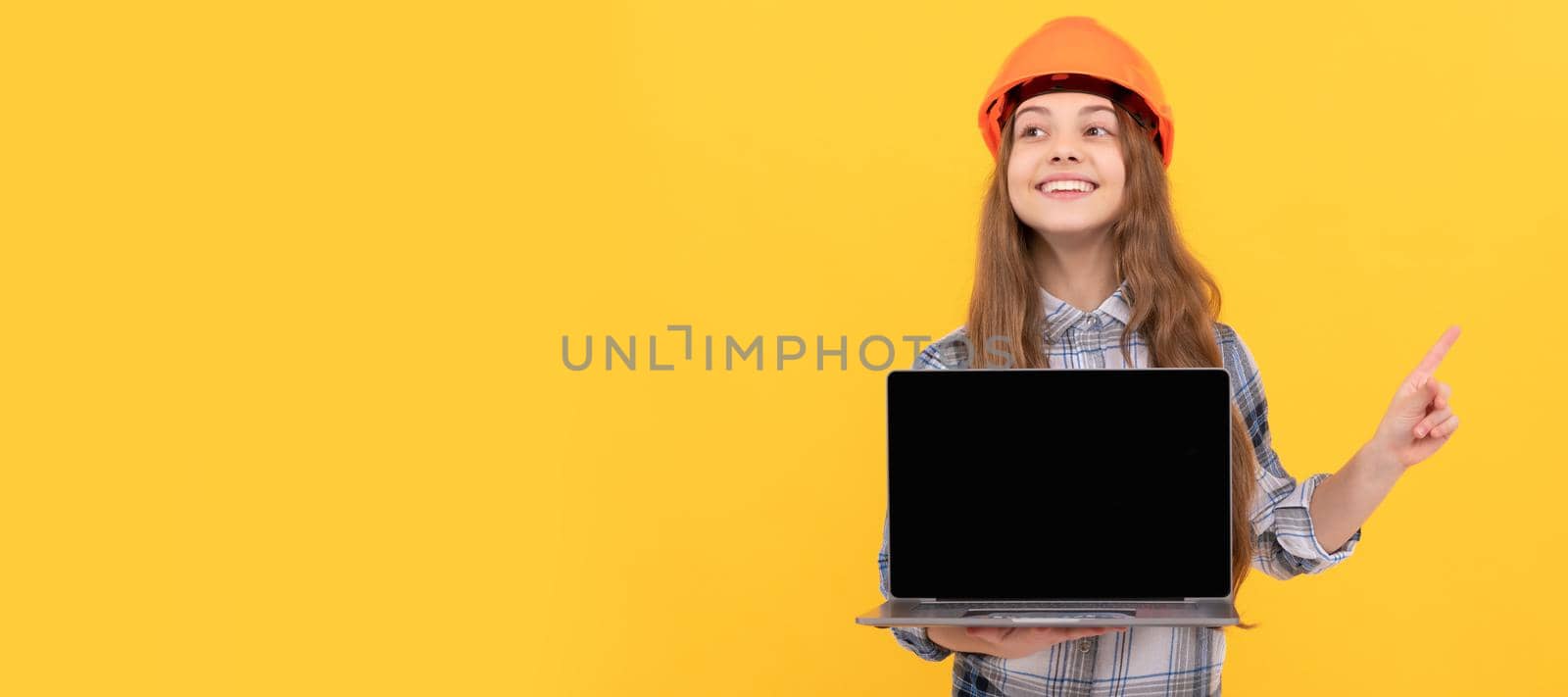 happy teen girl in helmet and checkered shirt presenting laptop pointing finger, promotion. Child builder in helmet horizontal poster design. Banner header, copy space