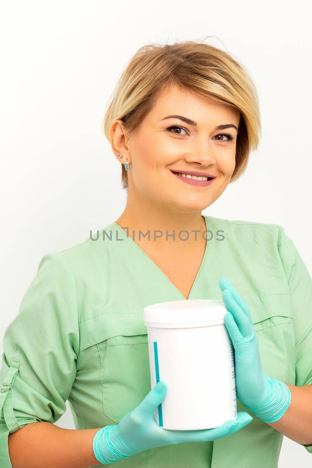 Cosmetics creams and skin care products in the hands of the female beautician smiling and standing over the white wall background. by okskukuruza
