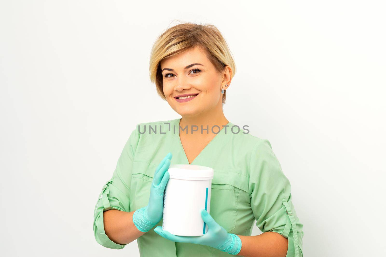 Cosmetics creams and skin care products in the hands of the female beautician smiling and standing over the white wall background. by okskukuruza