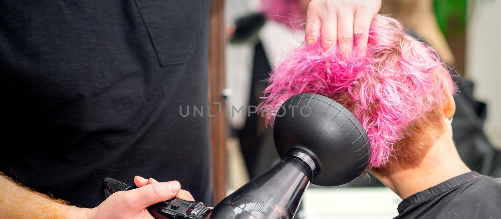 Drying short pink bob hairstyle of a young caucasian woman with a black hair dryer with the brush by hands of a male hairdresser in a hair salon, close up. by okskukuruza