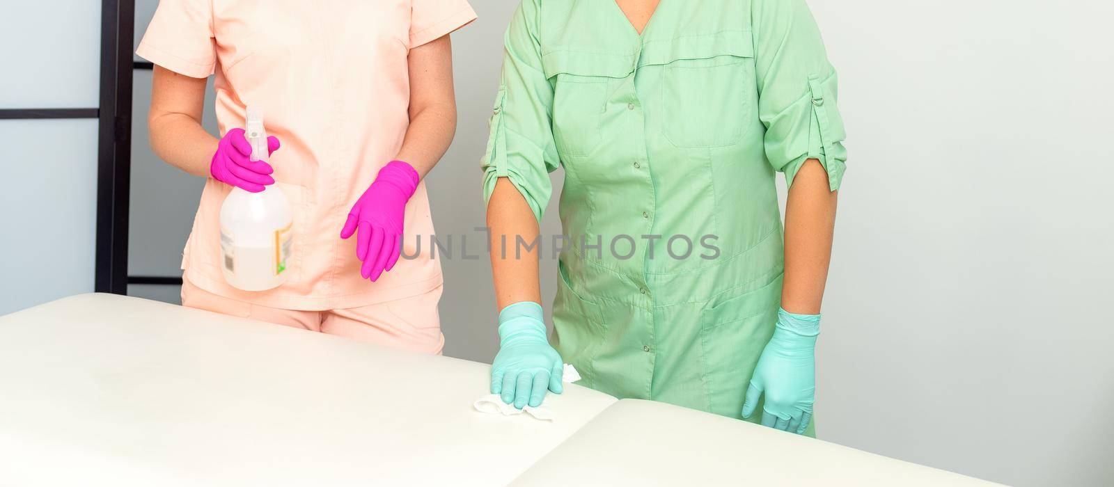 Two medical workers disinfect the patient's couch with sanitizer spray and a clean napkin. Health and hygiene concept. by okskukuruza