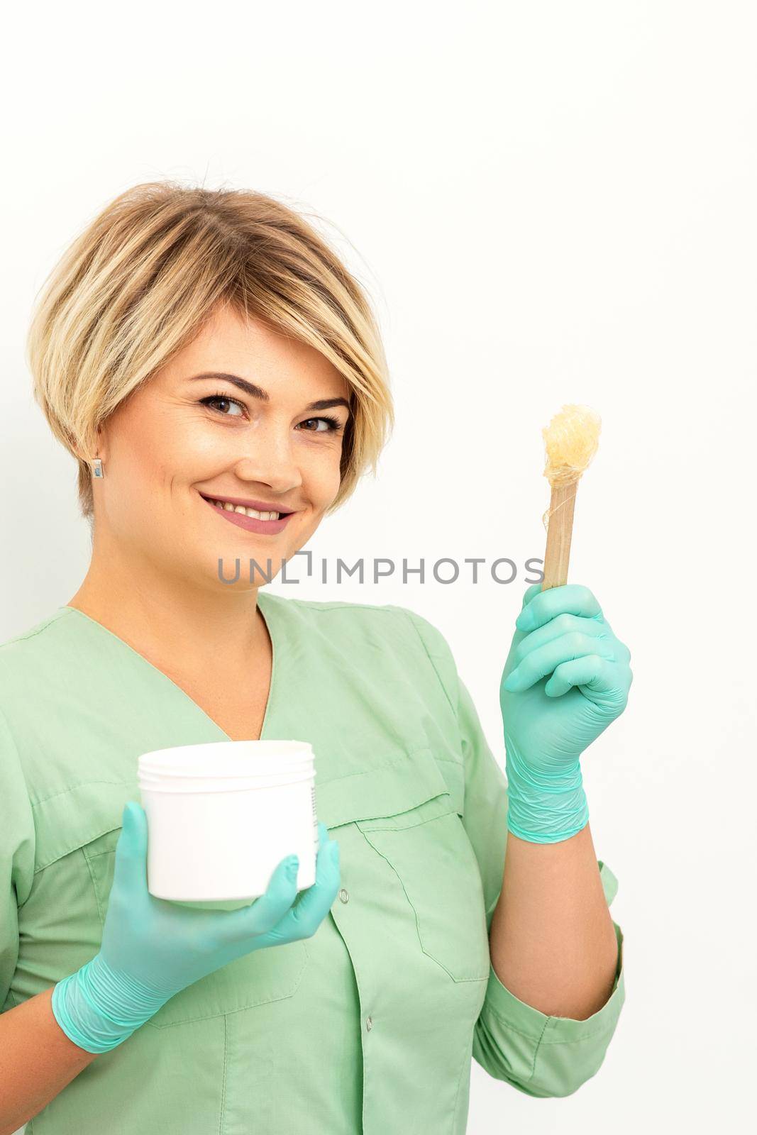 The master of sugar hair removal holds liquid yellow sugar paste, wax for depilation with the jar on a wooden stick on a white background