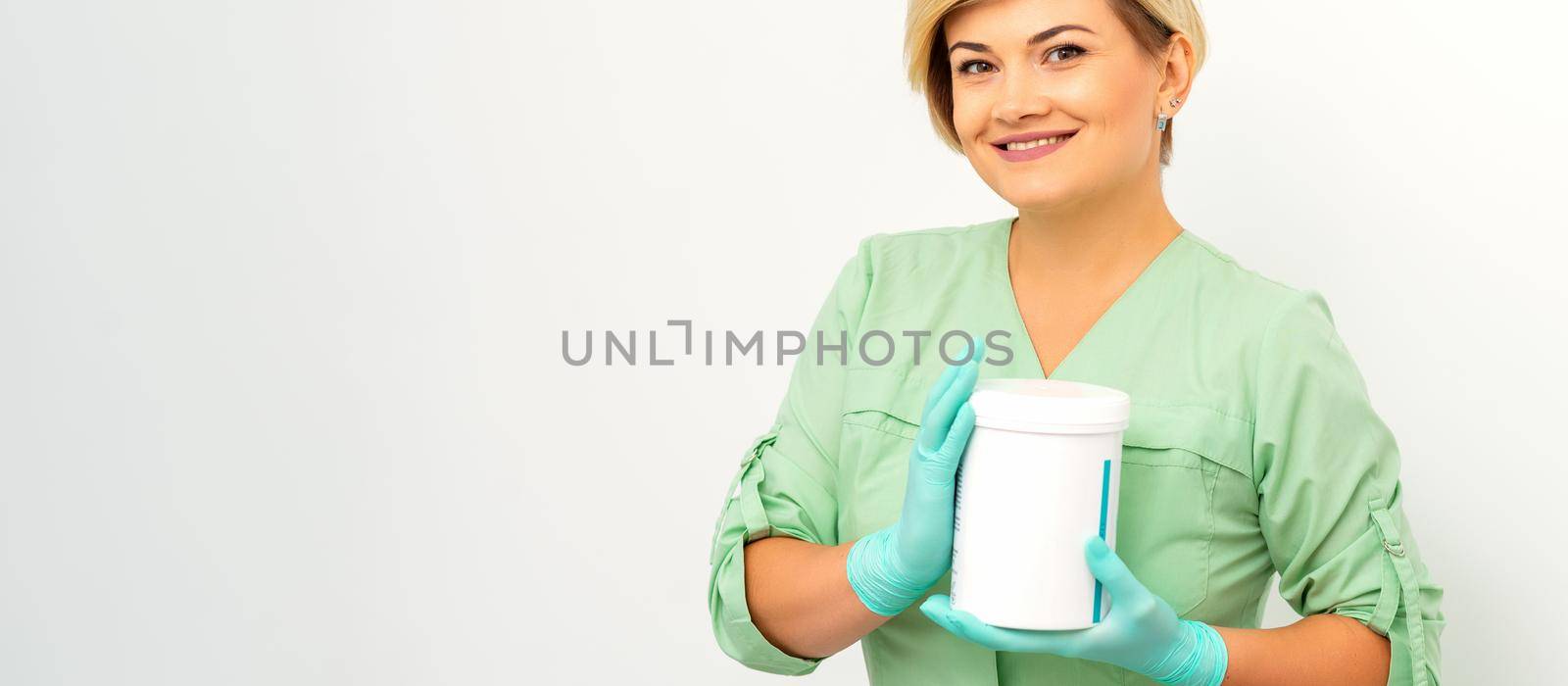 Cosmetics creams and skin care products in the hands of the female beautician smiling and standing over the white wall background