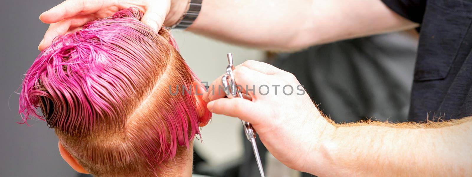 Haircut of dyed short pink wet hair of young caucasian woman by a male hairdresser in a barbershop