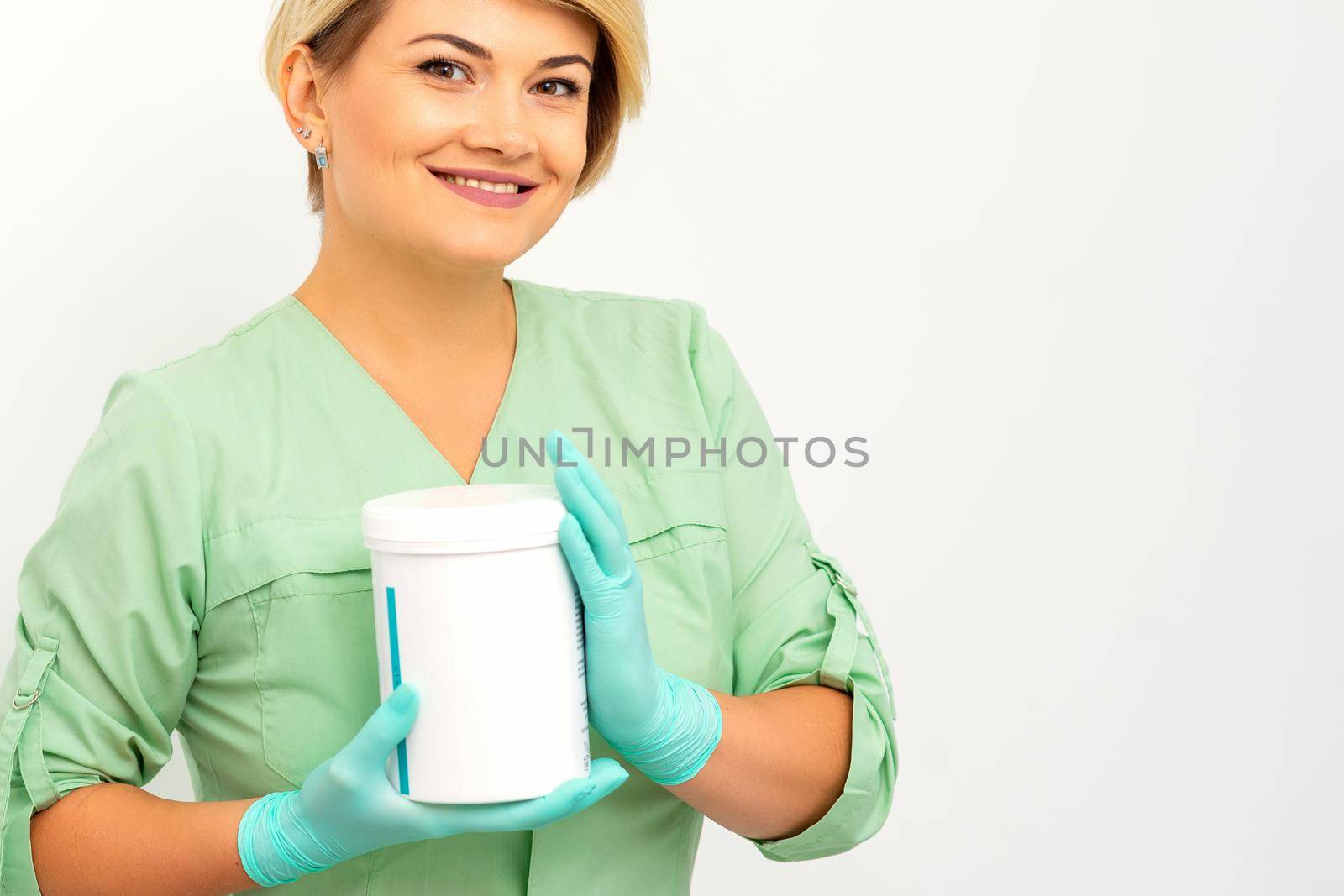 Cosmetics creams and skin care products in the hands of the female beautician smiling and standing over the white wall background