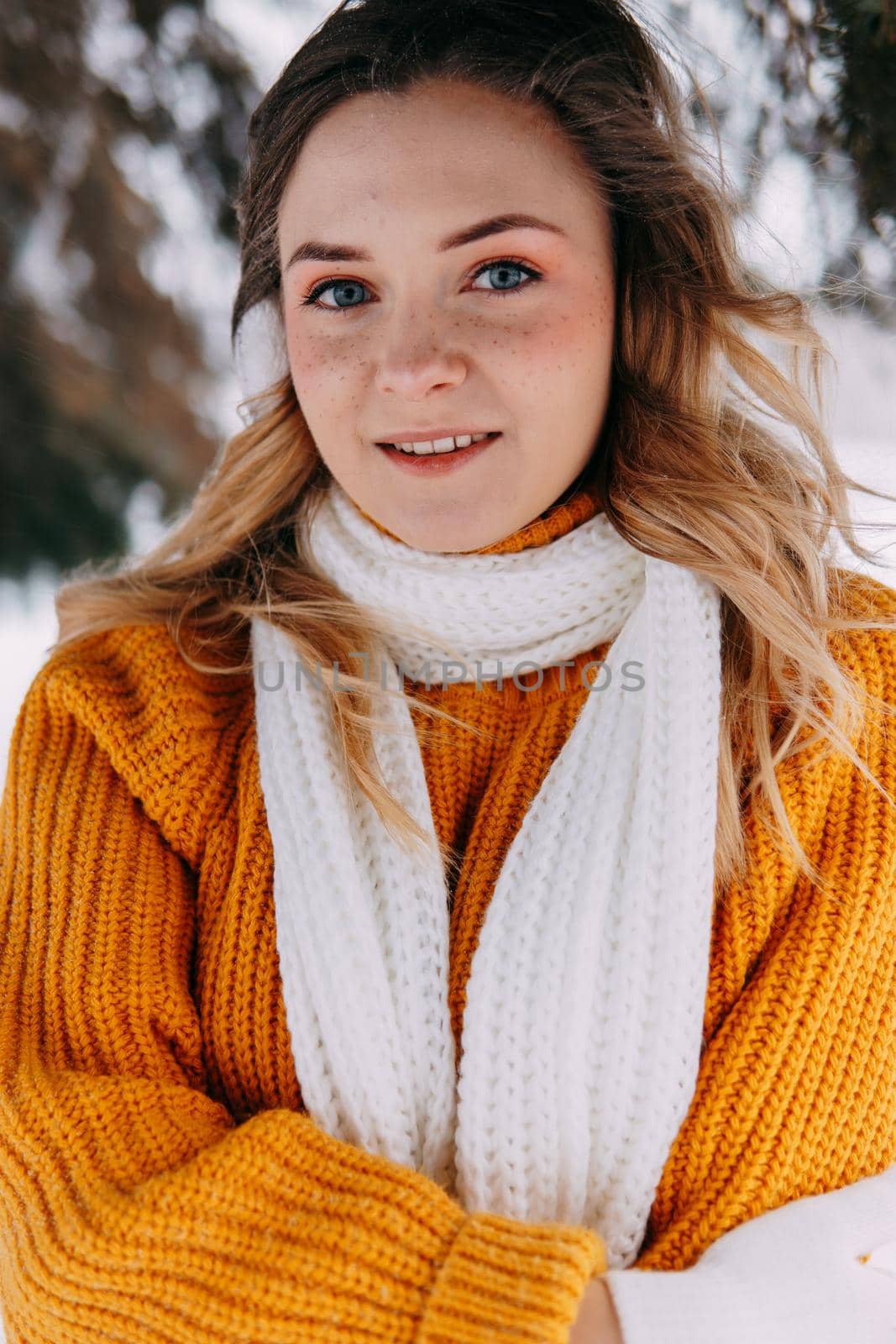 Teen blonde in a yellow sweater outside in winter. A teenage girl on a walk in winter clothes in a snowy forest.