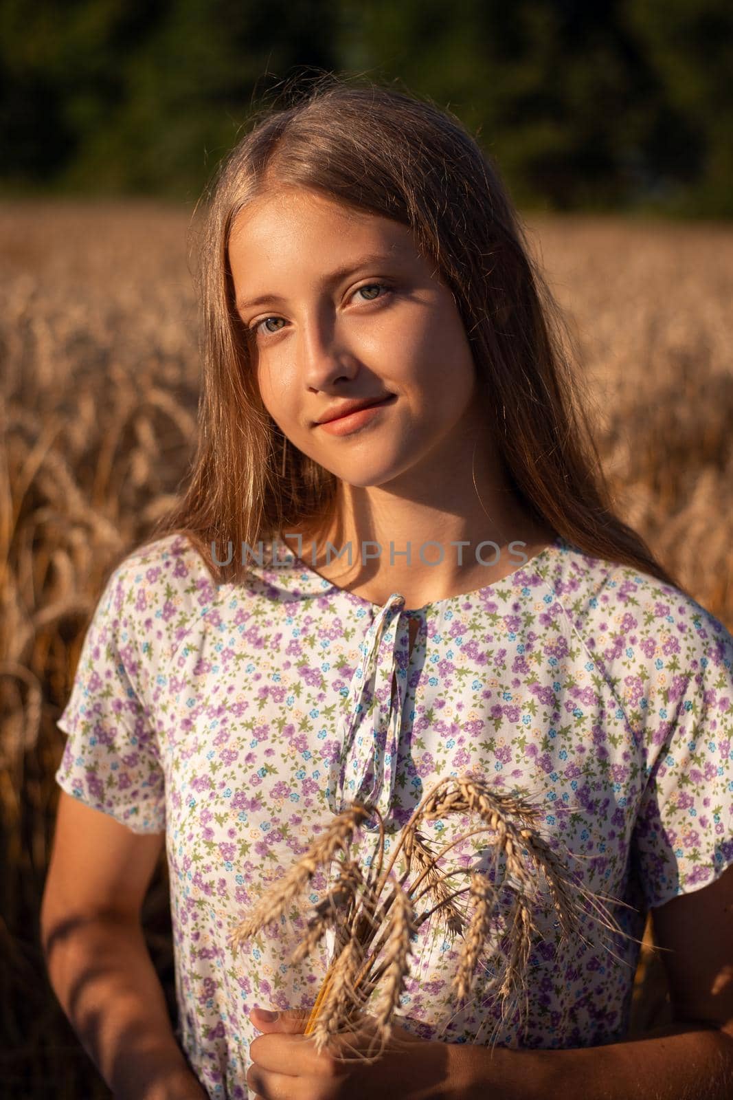 Portrait of beautiful smiling girl holding some rye ears sitting on the ground in the field of ripe wheat
