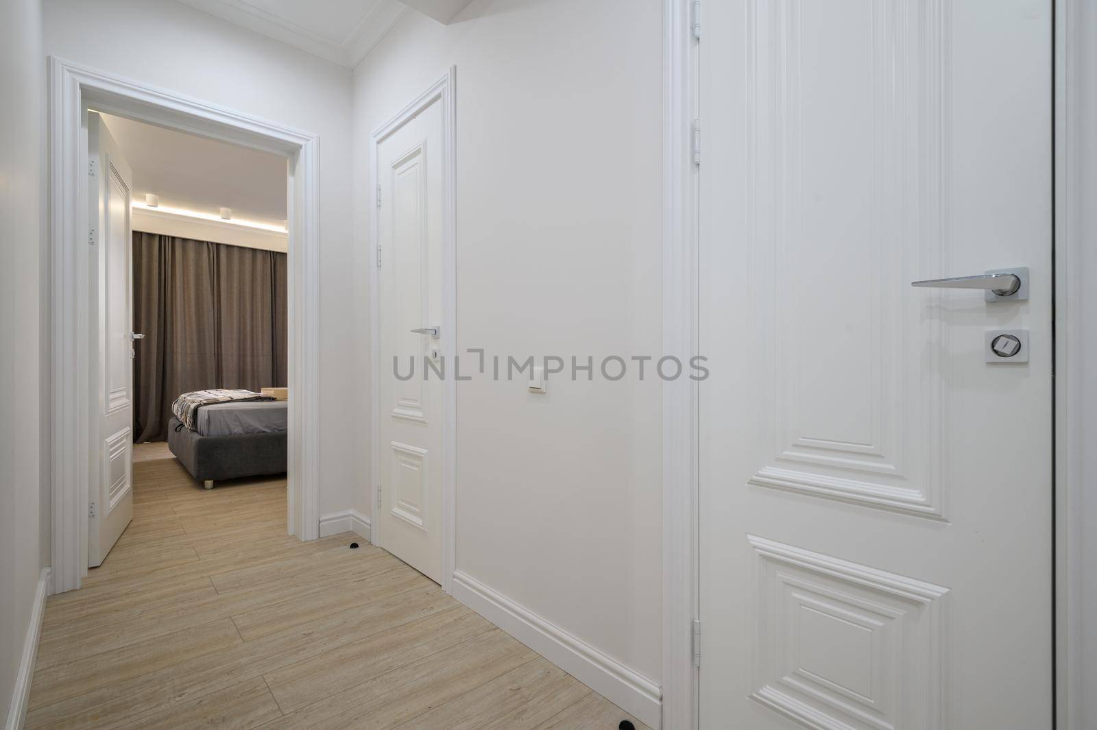 White hallway, door is open to a bedroom with a bed in the background