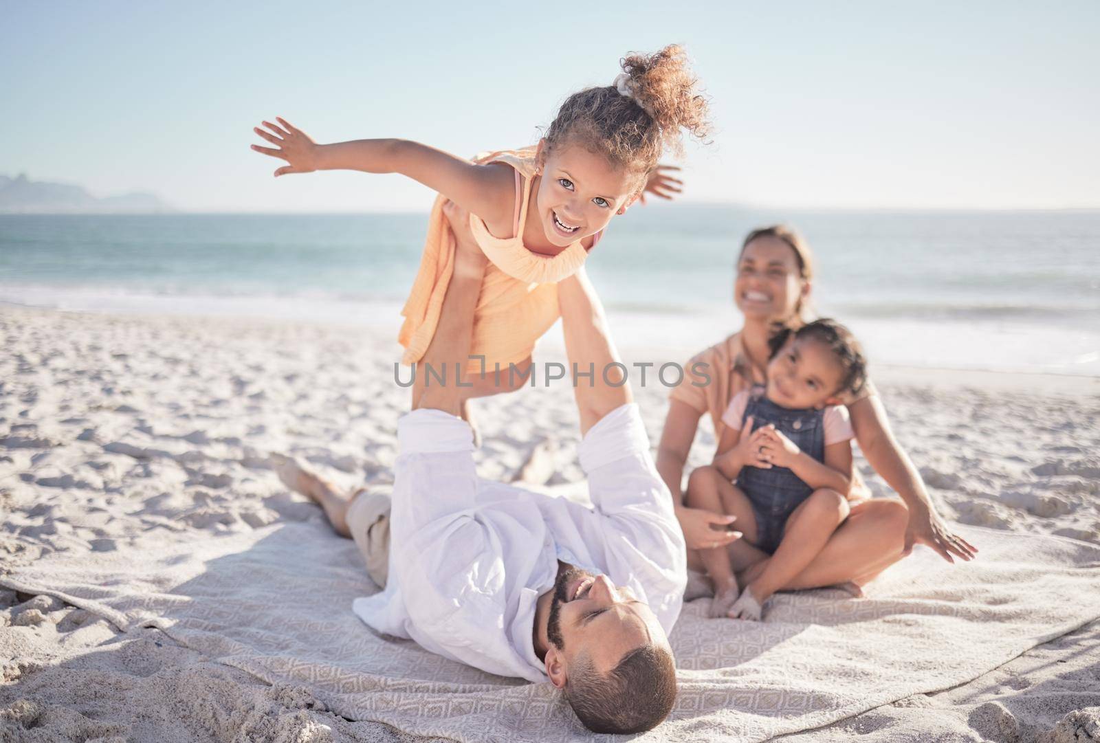 Family, children and playing with a girl on a beach holiday with her parents and sister during summer. Kids, travel and ocean with a female child or daughter on the sand by the sea with her father.