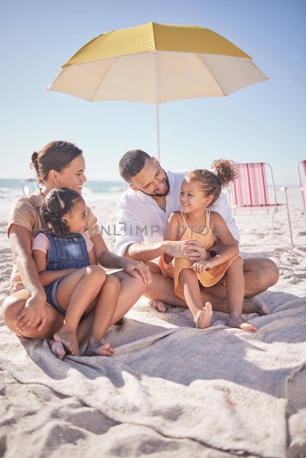 Family, happy and ocean summer experience of a mother, man and children enjoying the sea on sand. Happiness smile of kids and people together with quality time sitting in nature with a beach umbrella.
